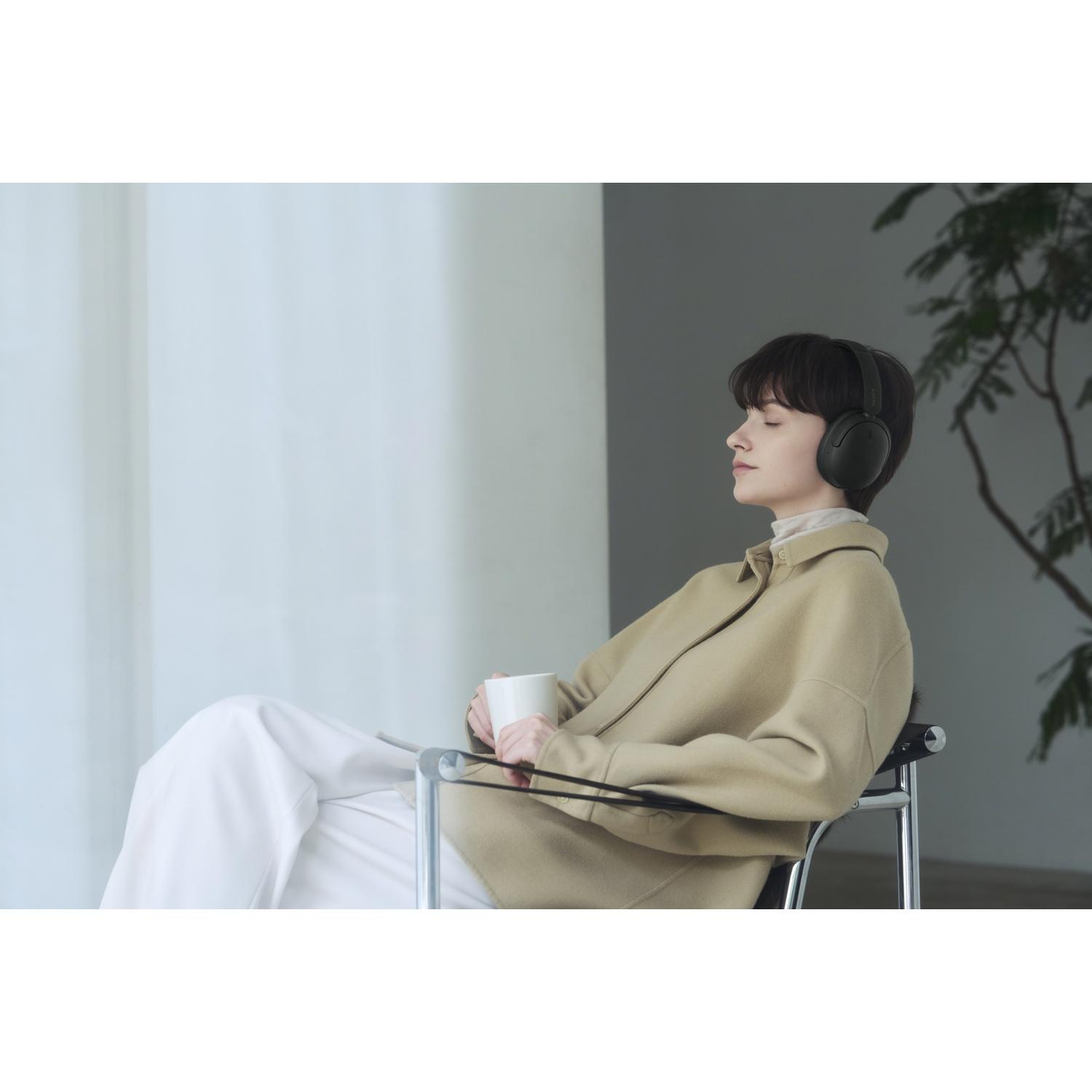 Une femme est assise dans un fauteuil moderne, yeux fermés, avec un casque et une tasse.