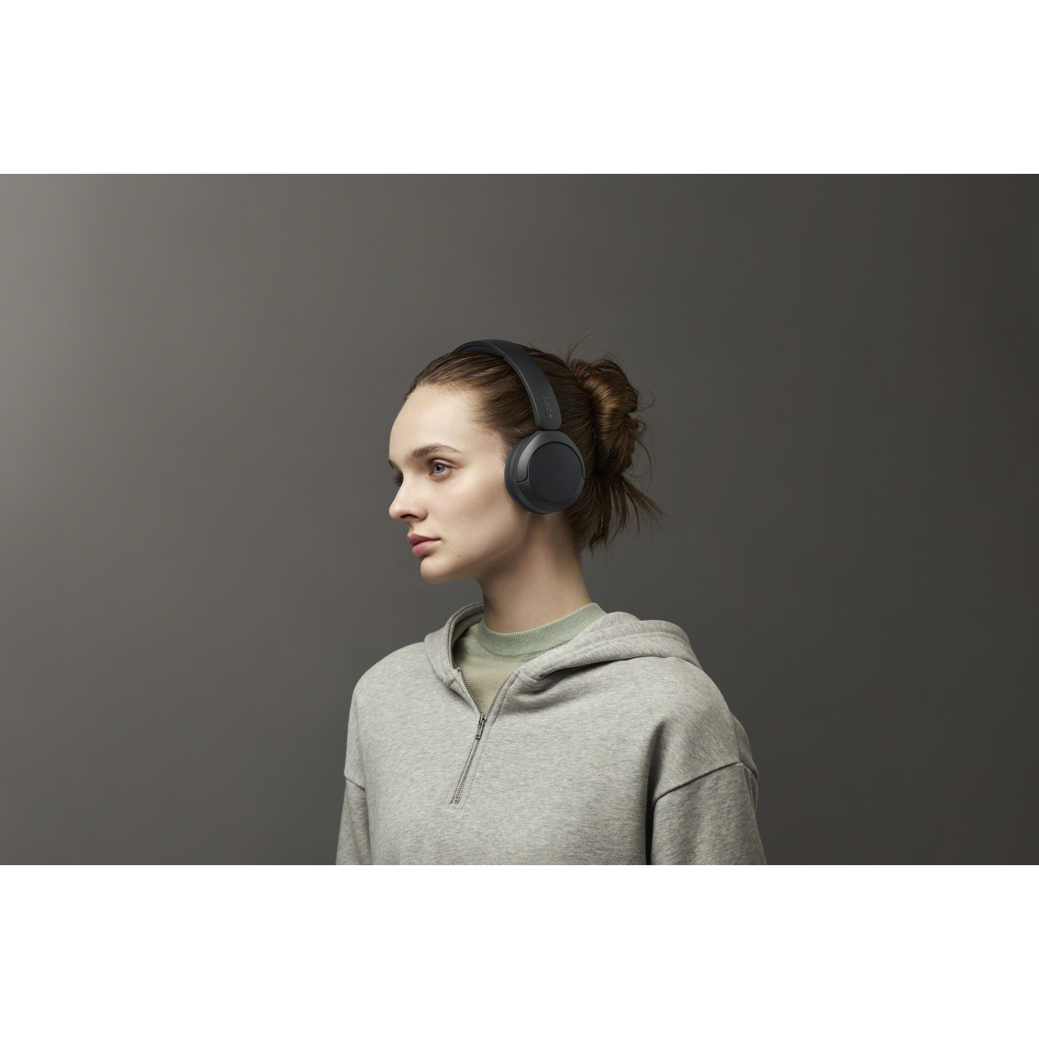Femme en sweat gris portant un casque noir sur fond gris.