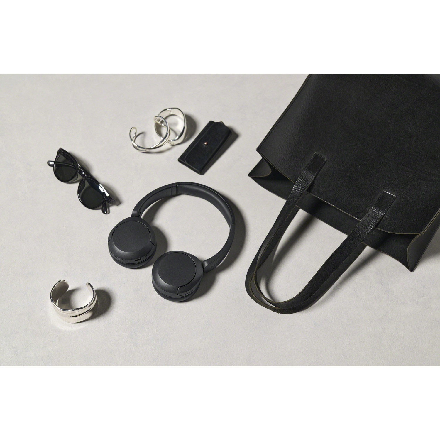 Un sac à main noir, un casque, des lunettes de soleil et des bijoux en argent sont disposés sur une surface claire.