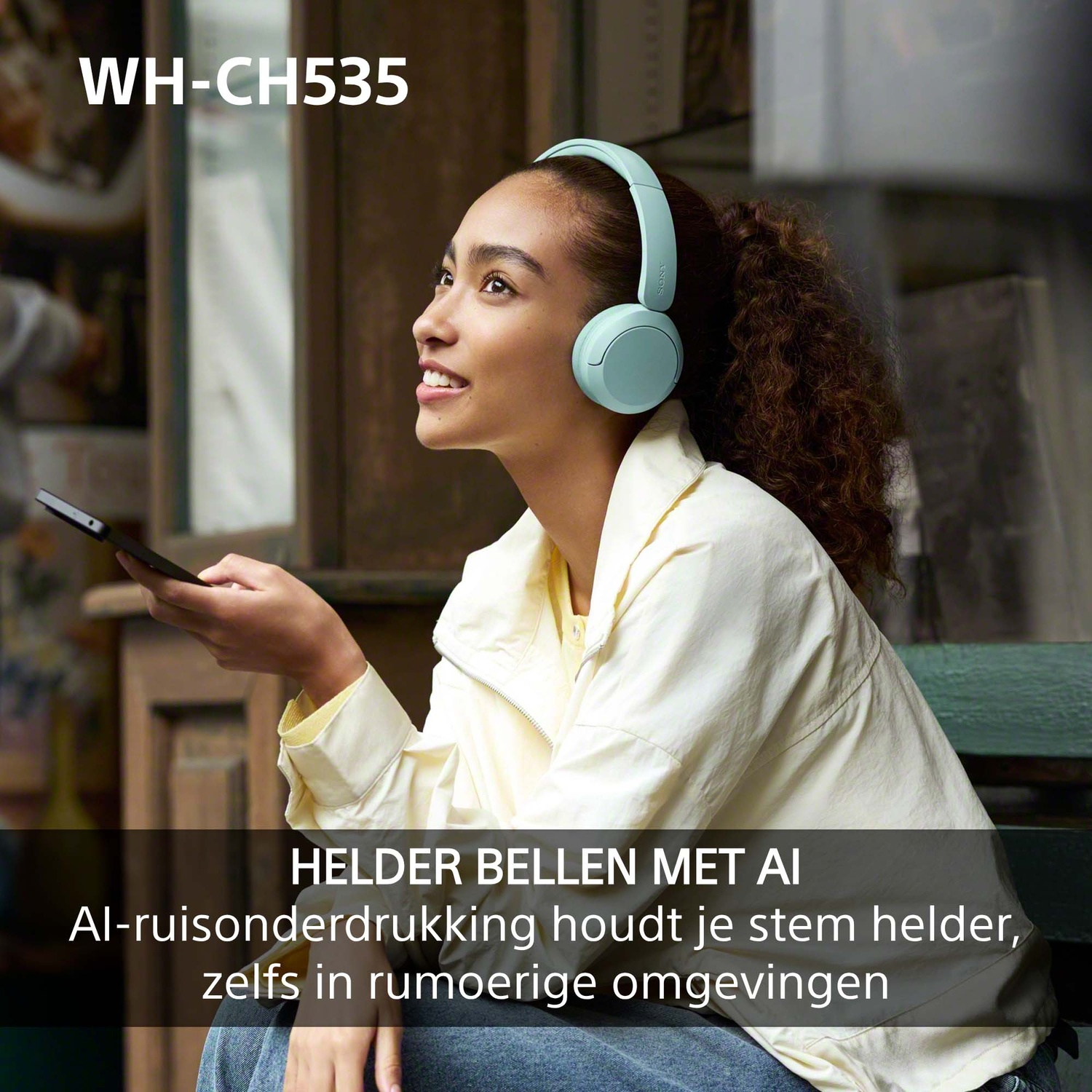 Een jonge vrouw met een blauwe koptelefoon glimlacht en houdt een smartphone vast in een houten interieur.