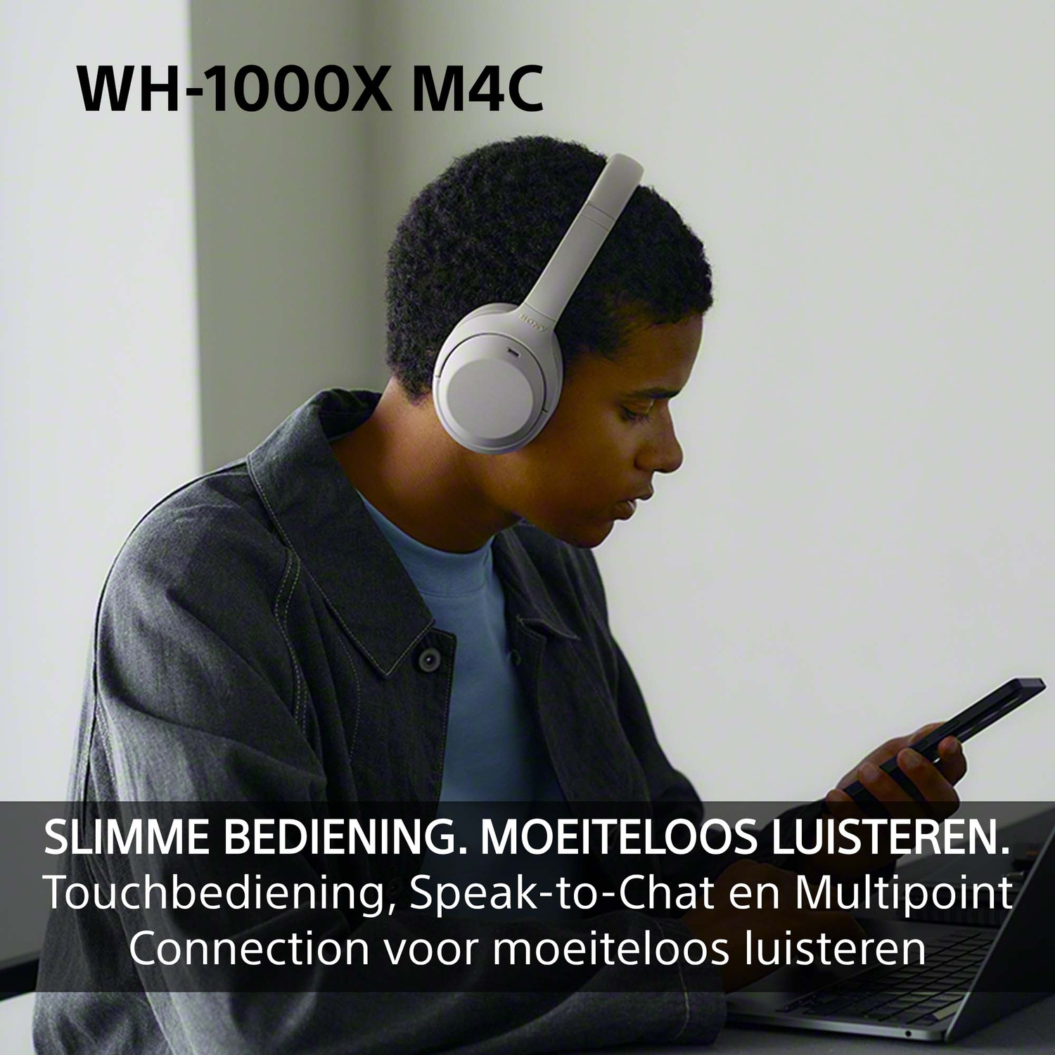 Een persoon met een witte koptelefoon gebruikt een smartphone en laptop in een kamer.
