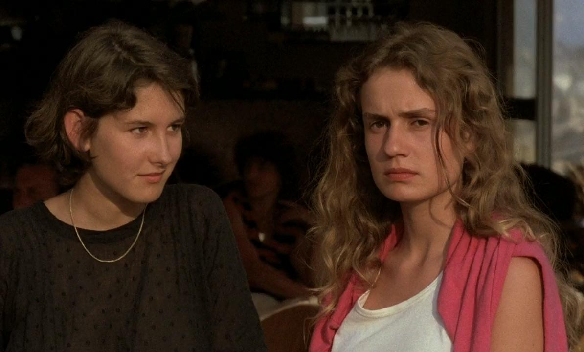 Zwei junge Frauen mit ernstem Gesichtsausdruck blicken in verschiedene Richtungen in einem Innenraum.