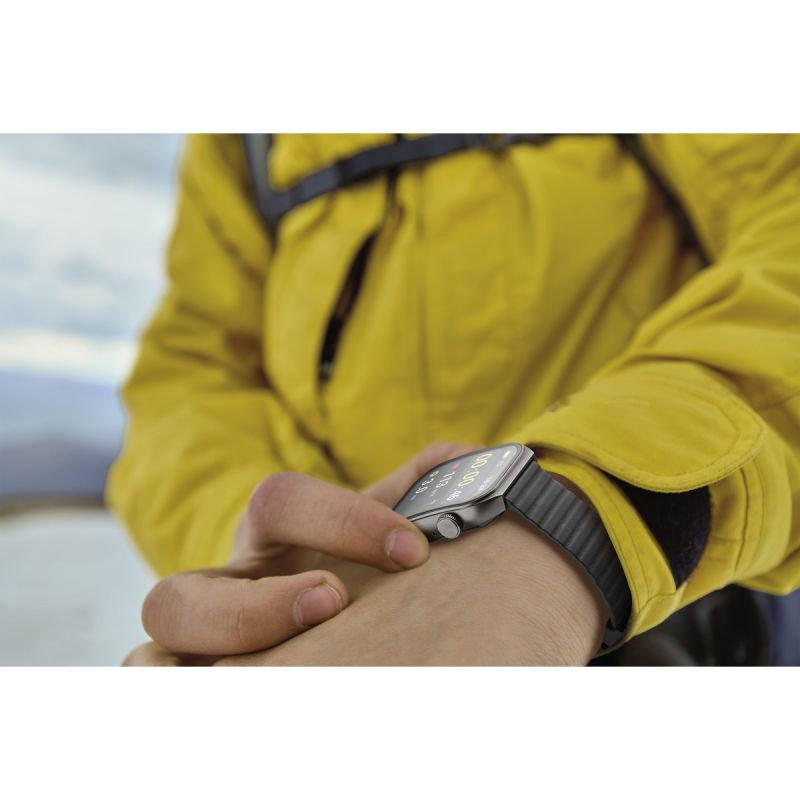 Person mit gelber Jacke bedient eine Smartwatch am Handgelenk in der Natur.