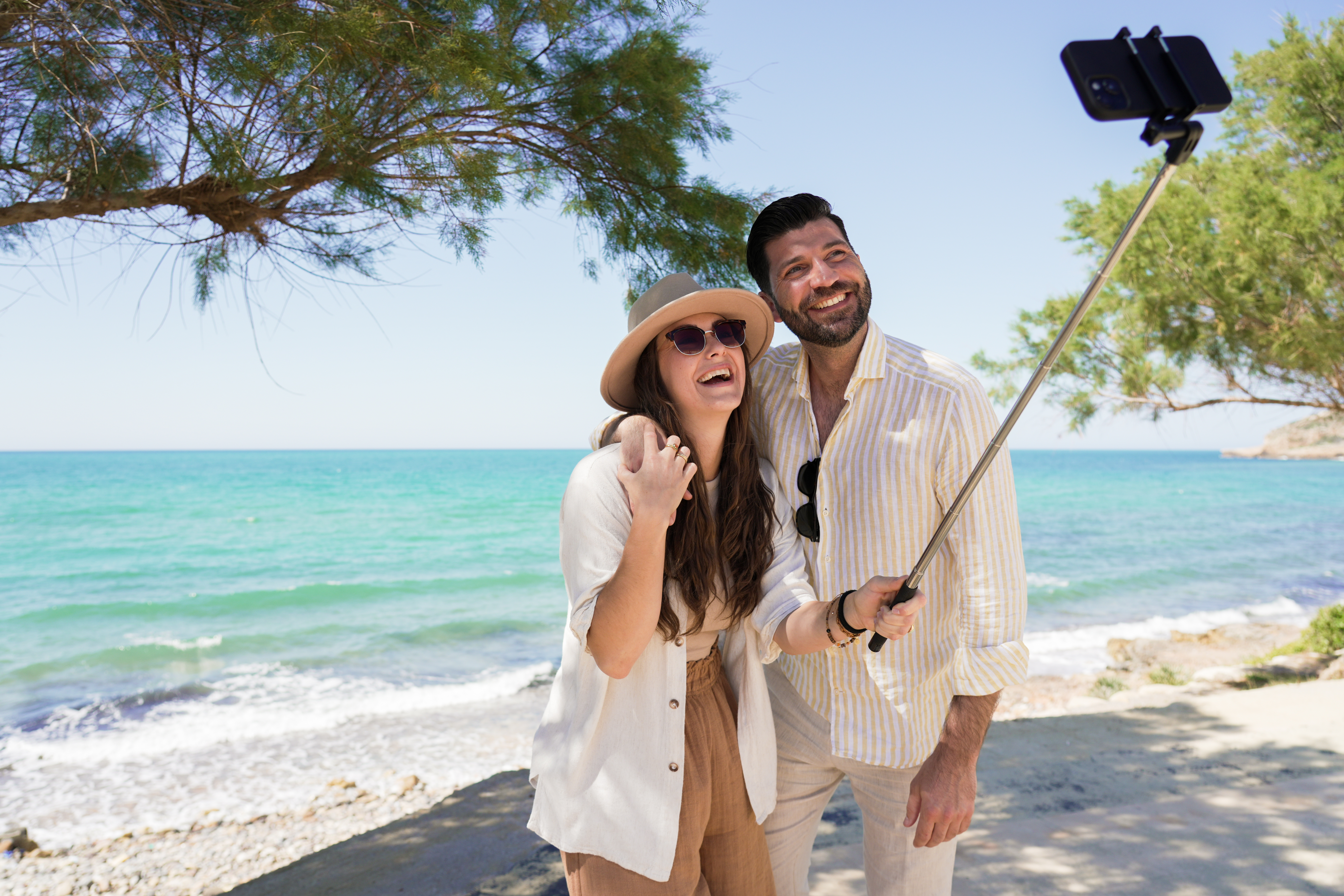 Couple heureux prenant un selfie sur une plage ensoleillée avec mer bleue.