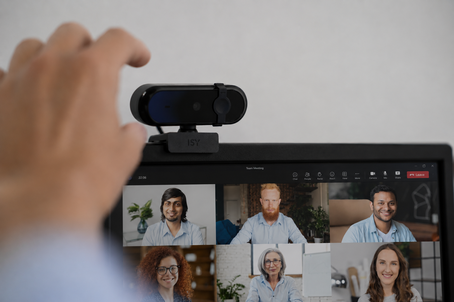 Una mano afferra una webcam montata su un monitor con una videochiamata.