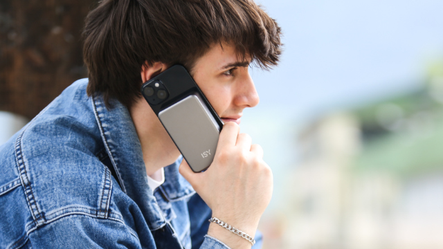 Un jeune homme en veste en jean téléphone en extérieur avec un smartphone doté d'une batterie externe grise.