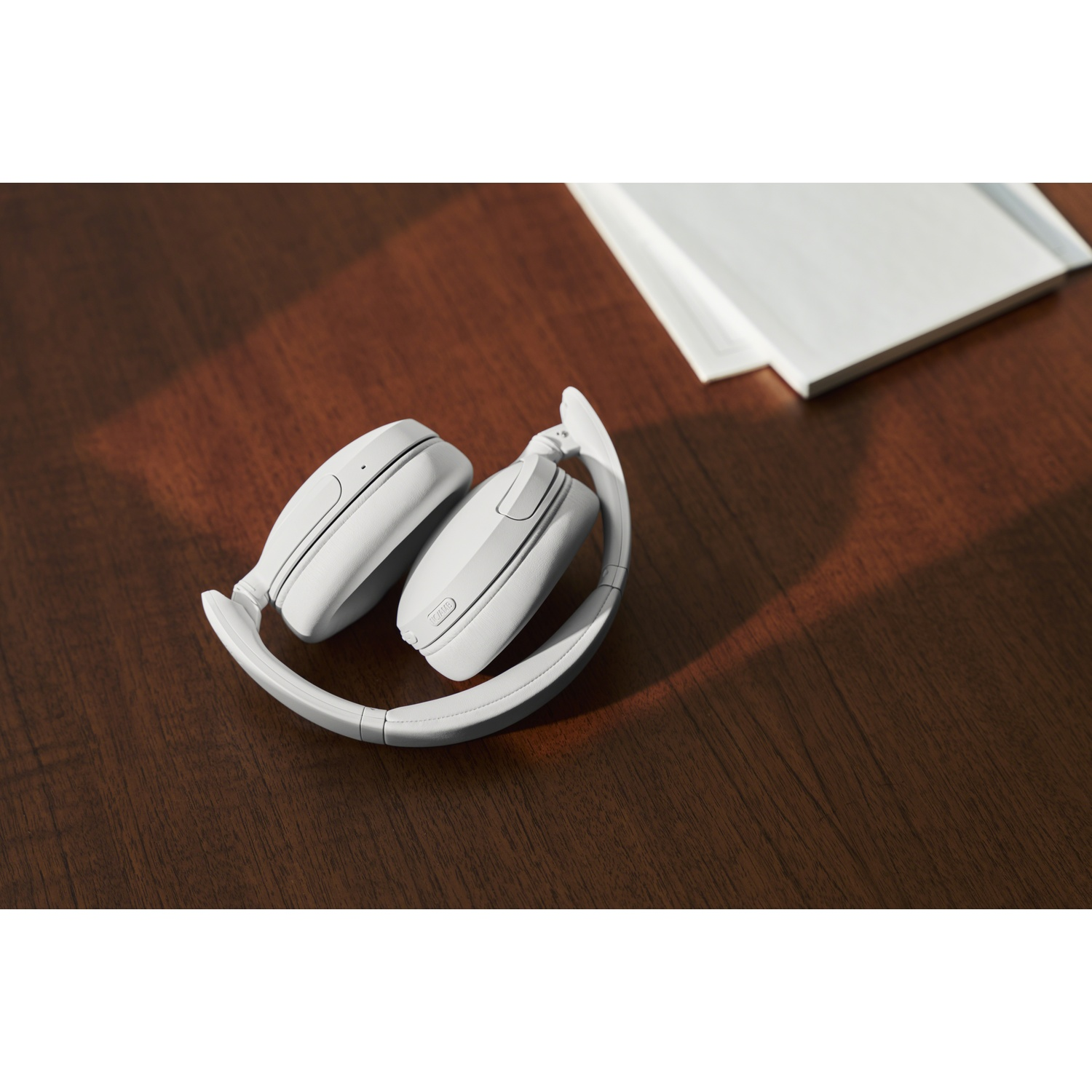 Des écouteurs blancs reposent sur une table en bois sombre à côté d'un carnet.