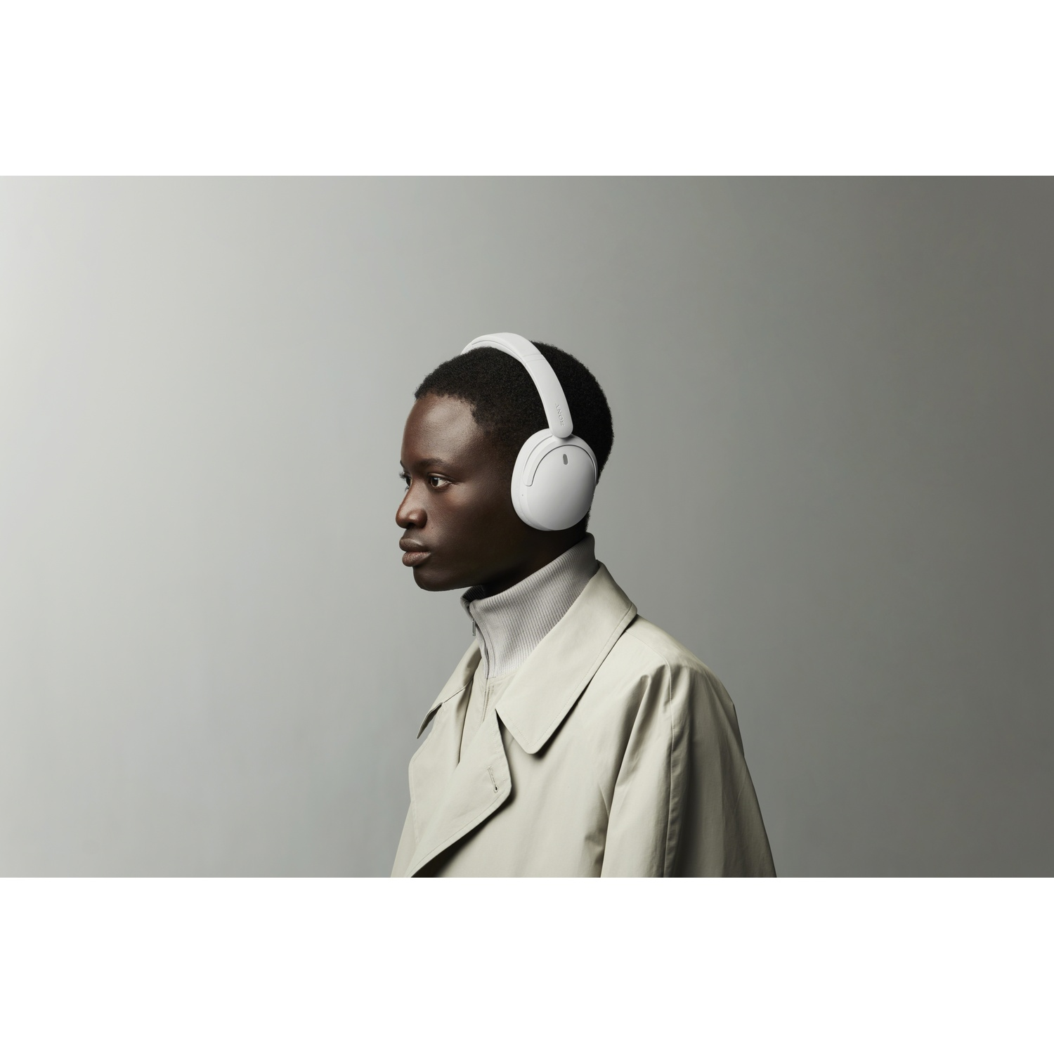 Profil d'une personne portant un casque blanc, un manteau clair et un col roulé gris sur fond gris.