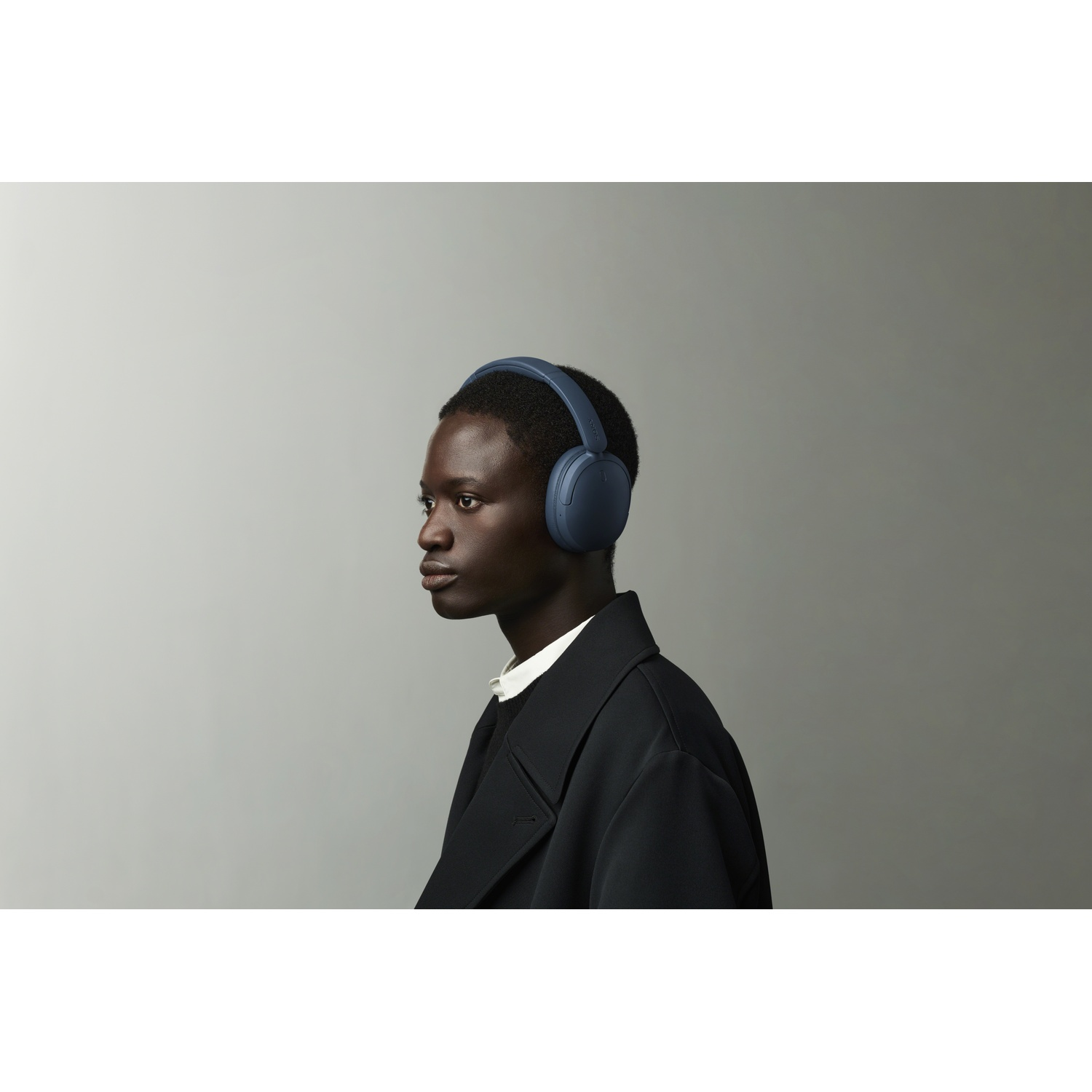 Une personne portant un casque bleu et un manteau noir regarde de côté sur un fond gris.