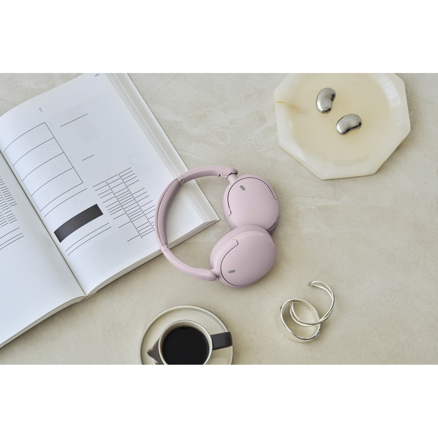 Casque rose à côté d'un carnet ouvert, de café et de petits objets décoratifs sur une table.