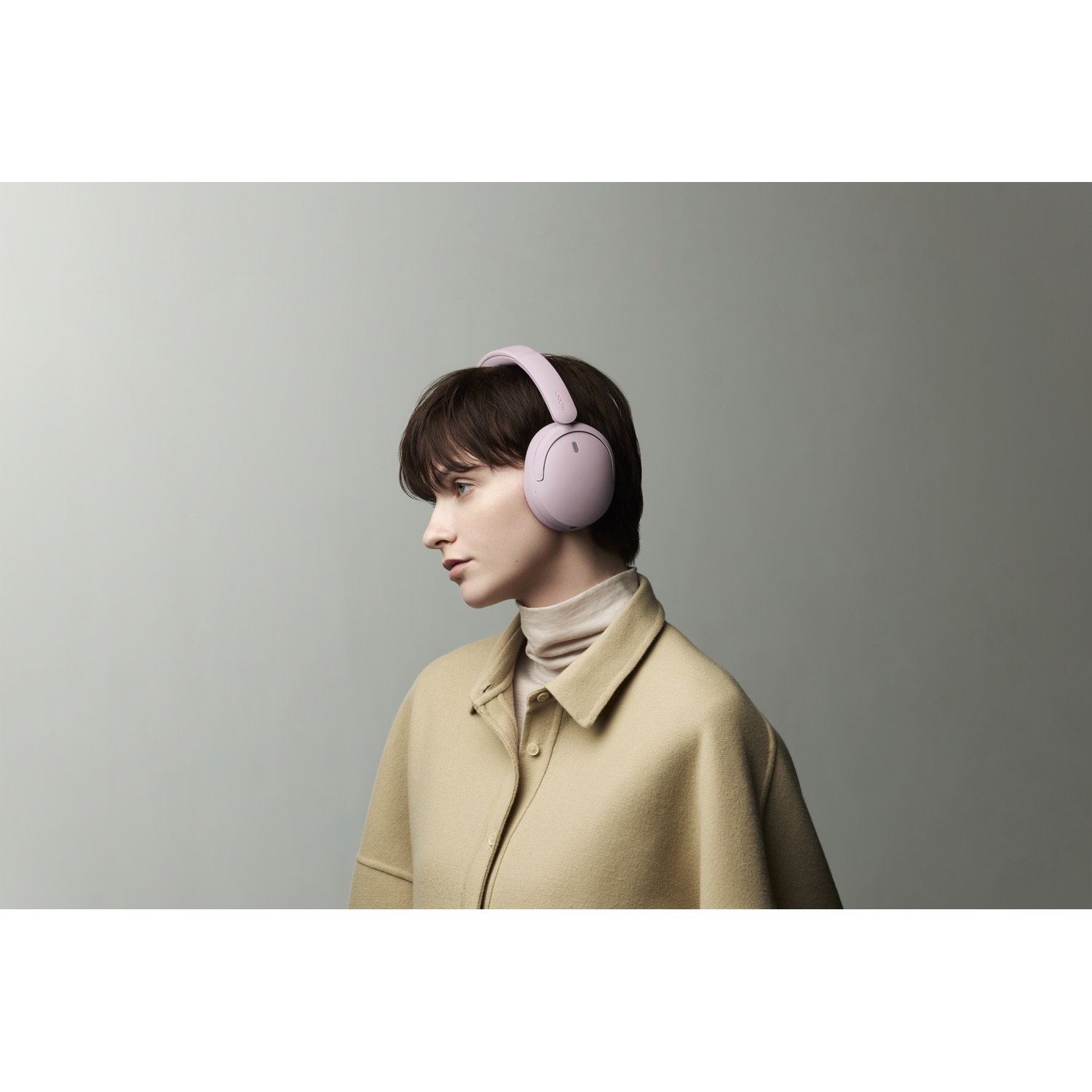 Femme aux cheveux bruns courts portant un casque rose et une veste beige sur fond gris.