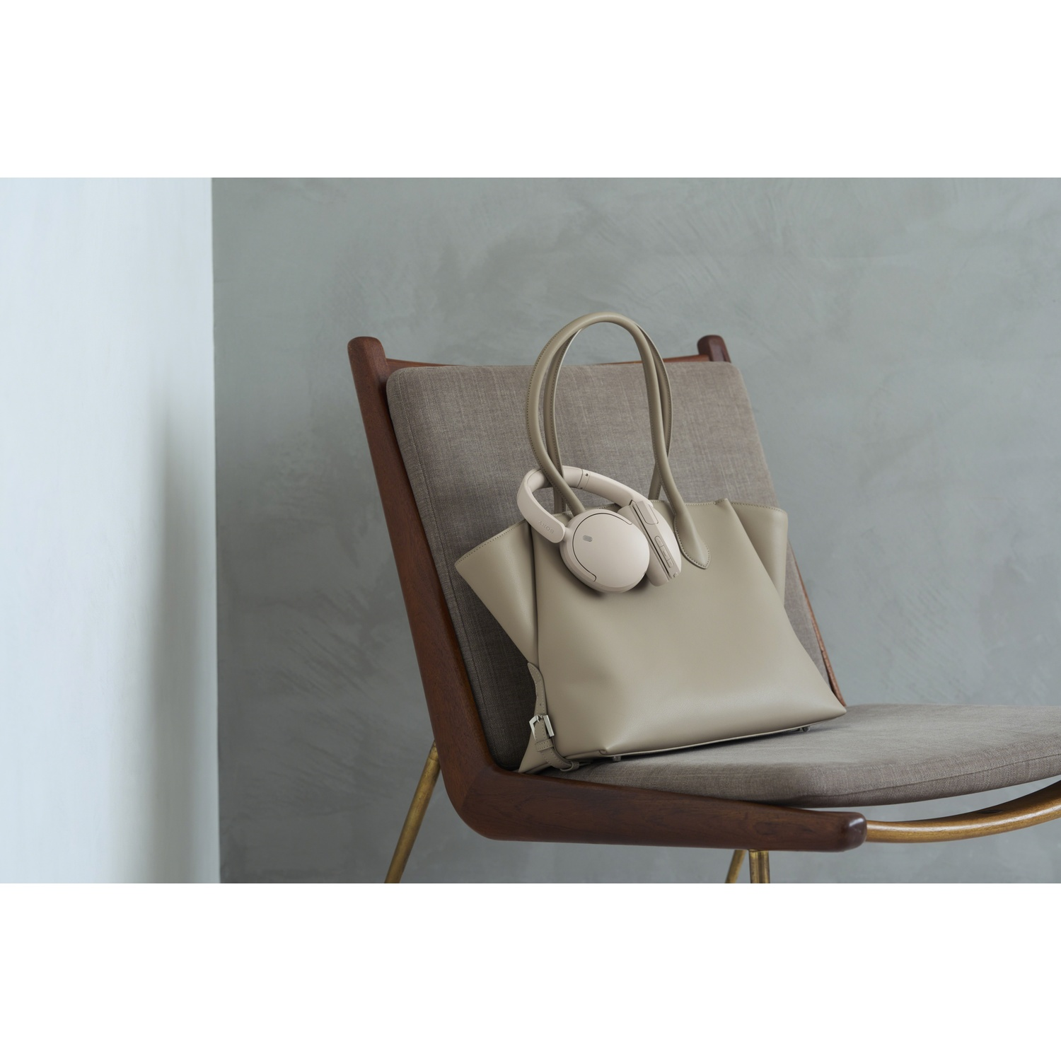 Sac à main beige avec des écouteurs sur une chaise en bois contre un mur gris.