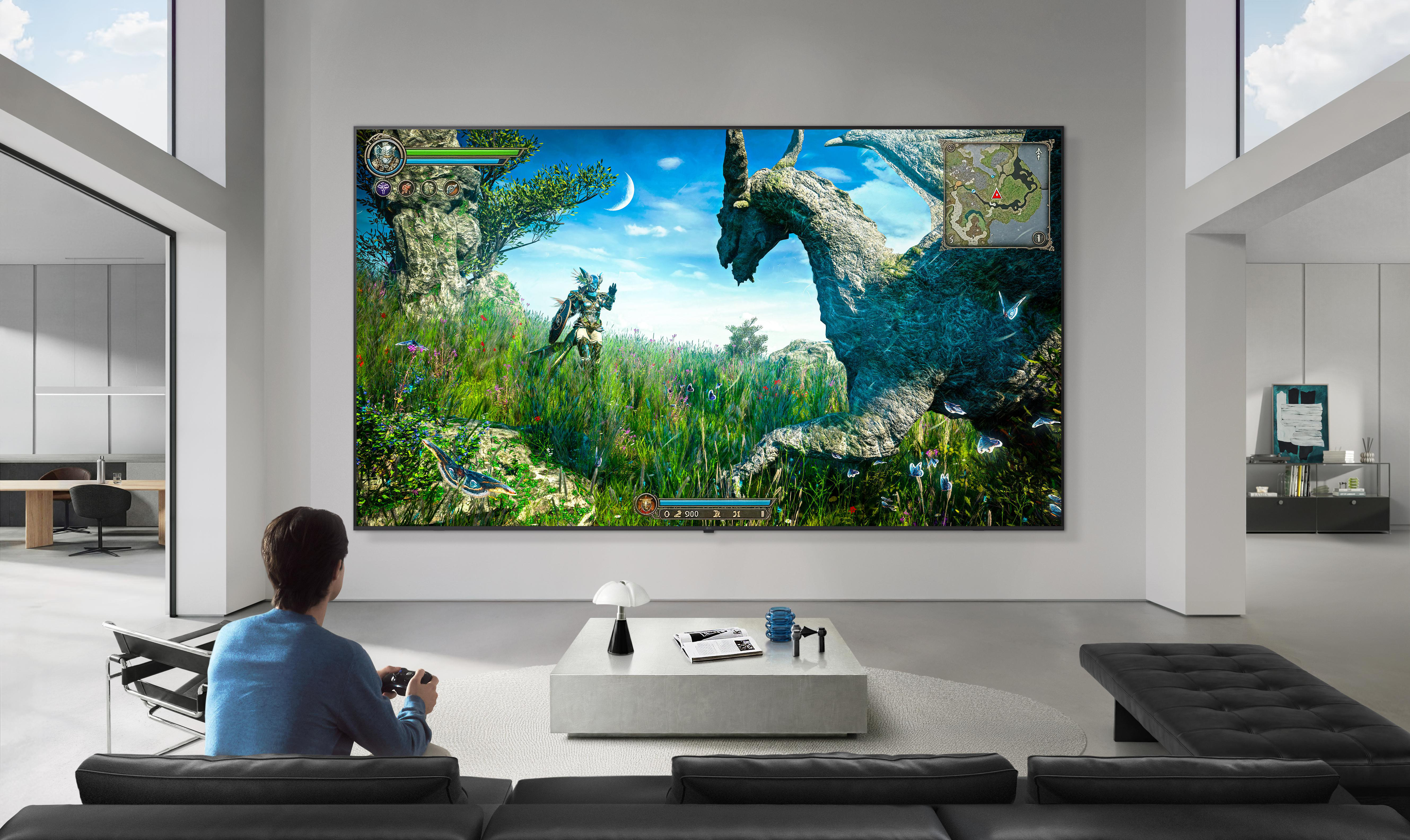 Ein Mann spielt ein Fantasy-Videospiel auf einem großen Fernseher in einem hellen, modernen Wohnzimmer.