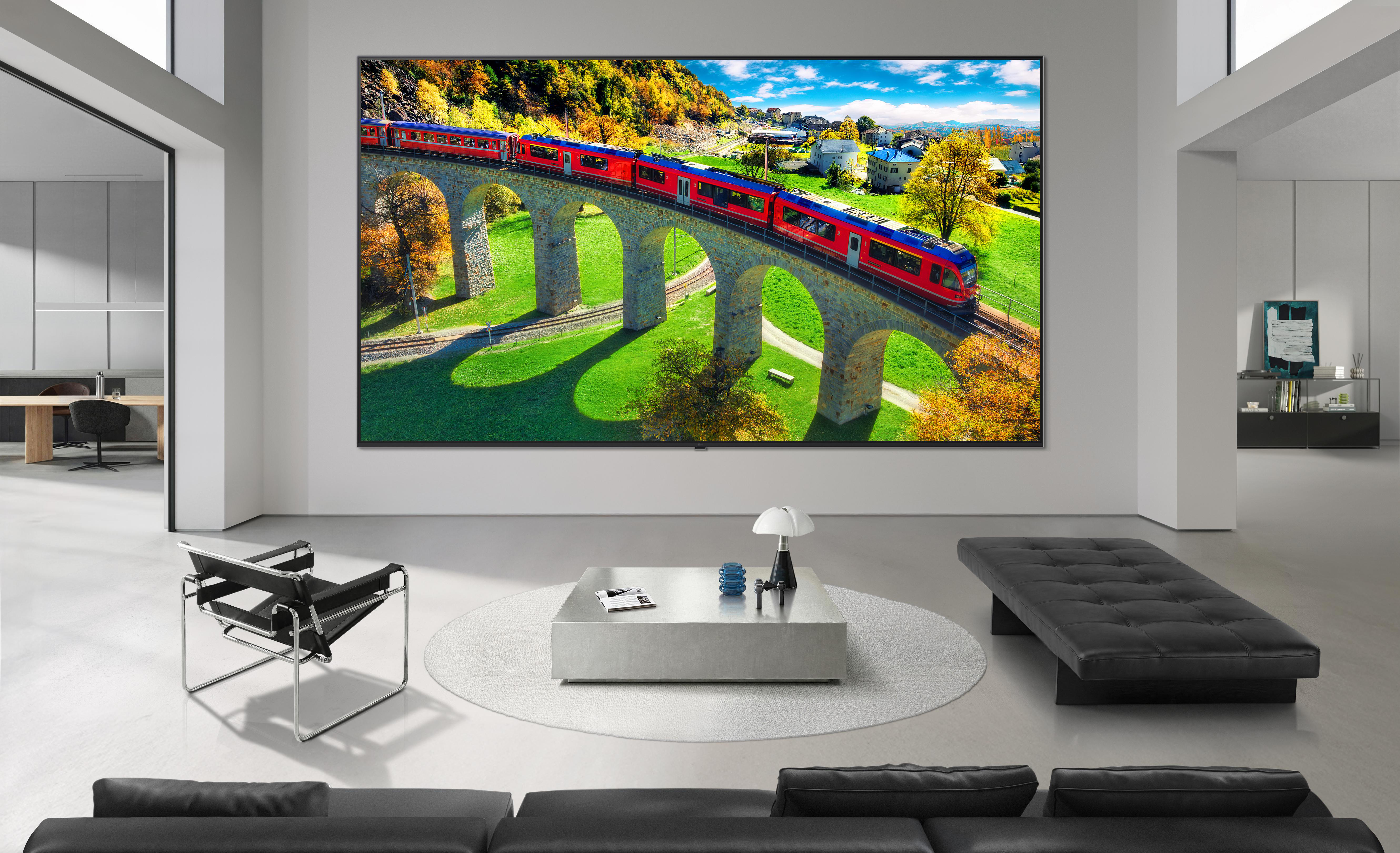 Moderne Wohnzimmer mit großem TV, der einen roten Zug auf einem Steinviadukt über grünen Feldern zeigt.