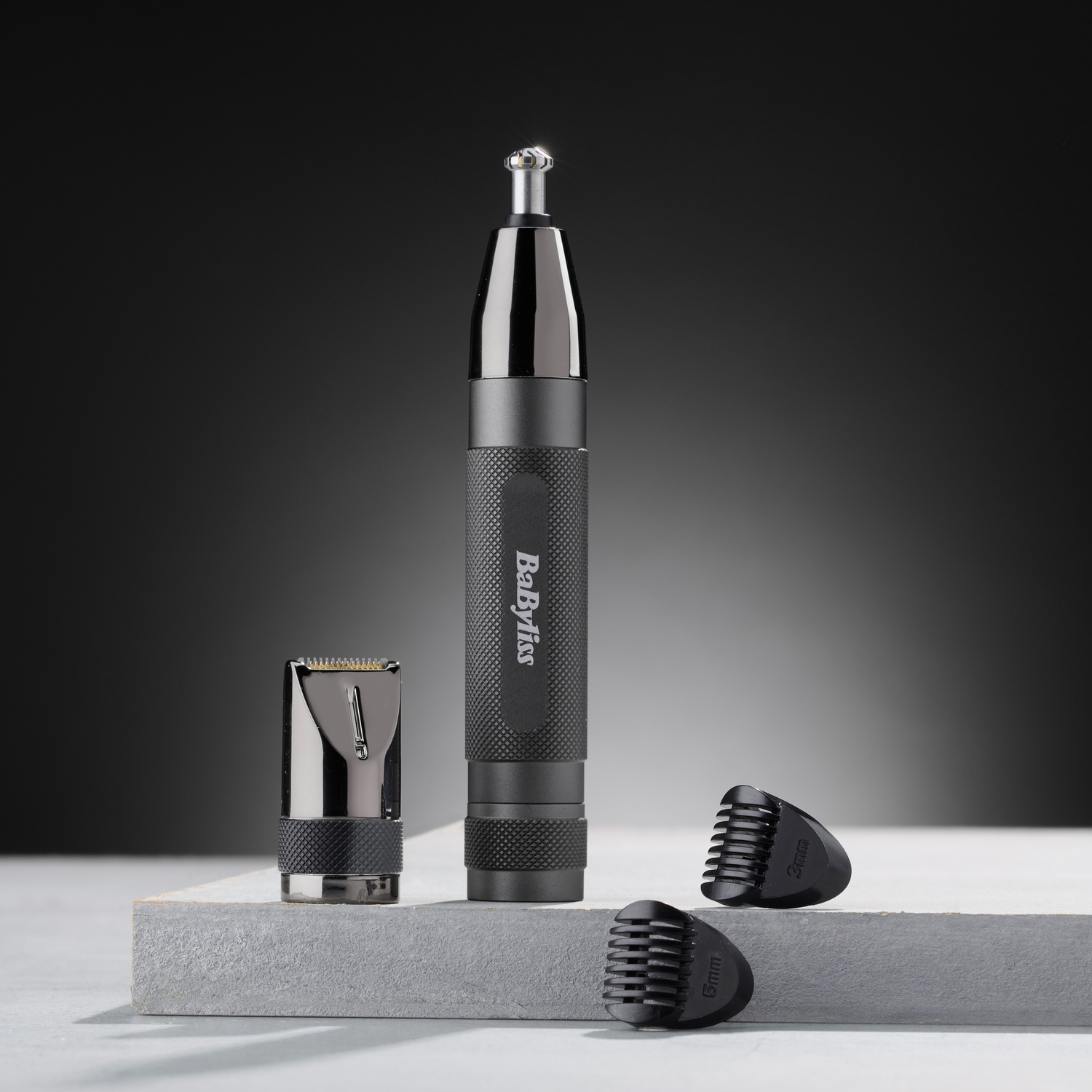 Regolabarba nasale Babyliss nero con accessori e testine di taglio su superficie grigia e sfondo scuro.
