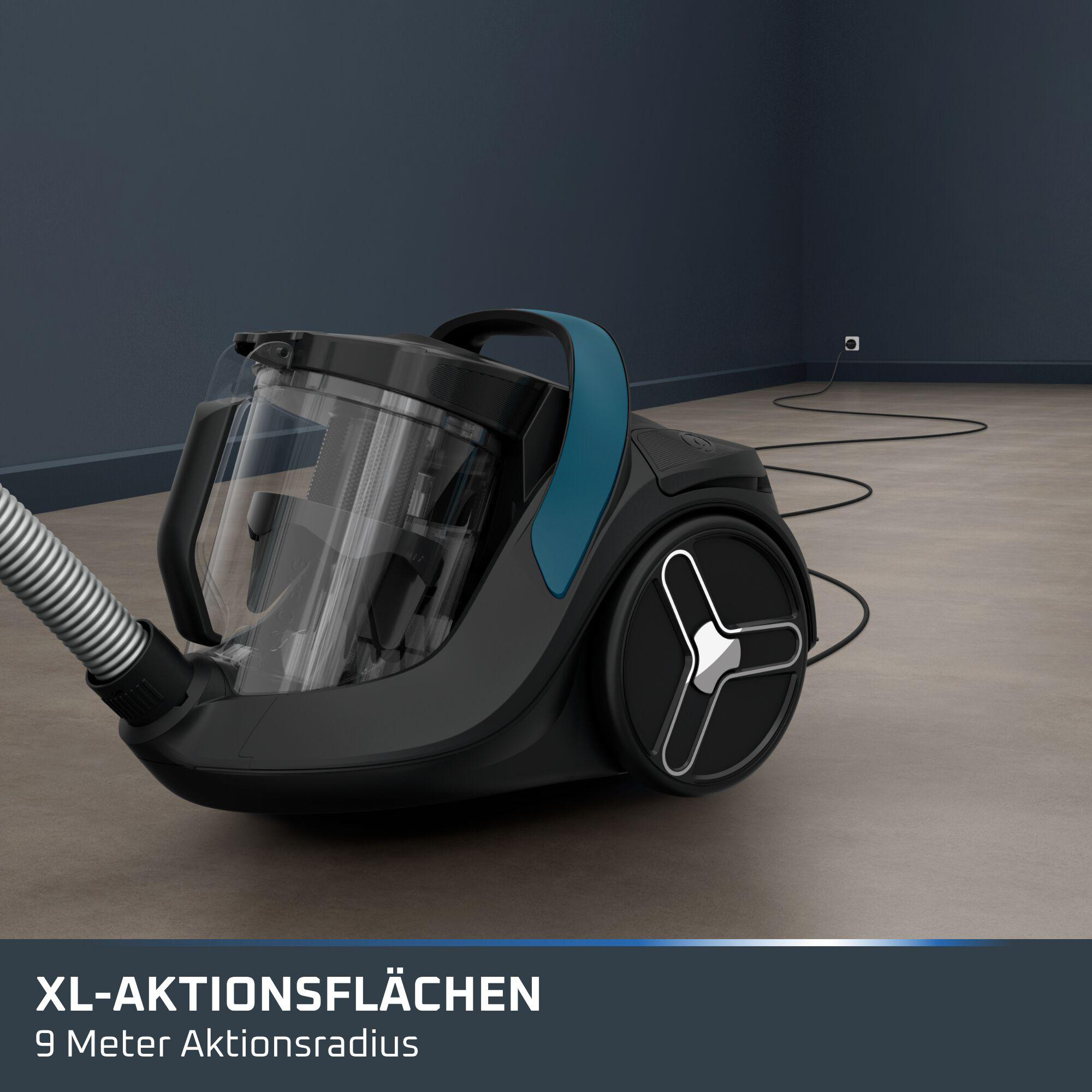 Schwarzer Staubsauger mit transparentem Staubbehälter und blauem Griff auf einem grauen Boden vor dunkler Wand.