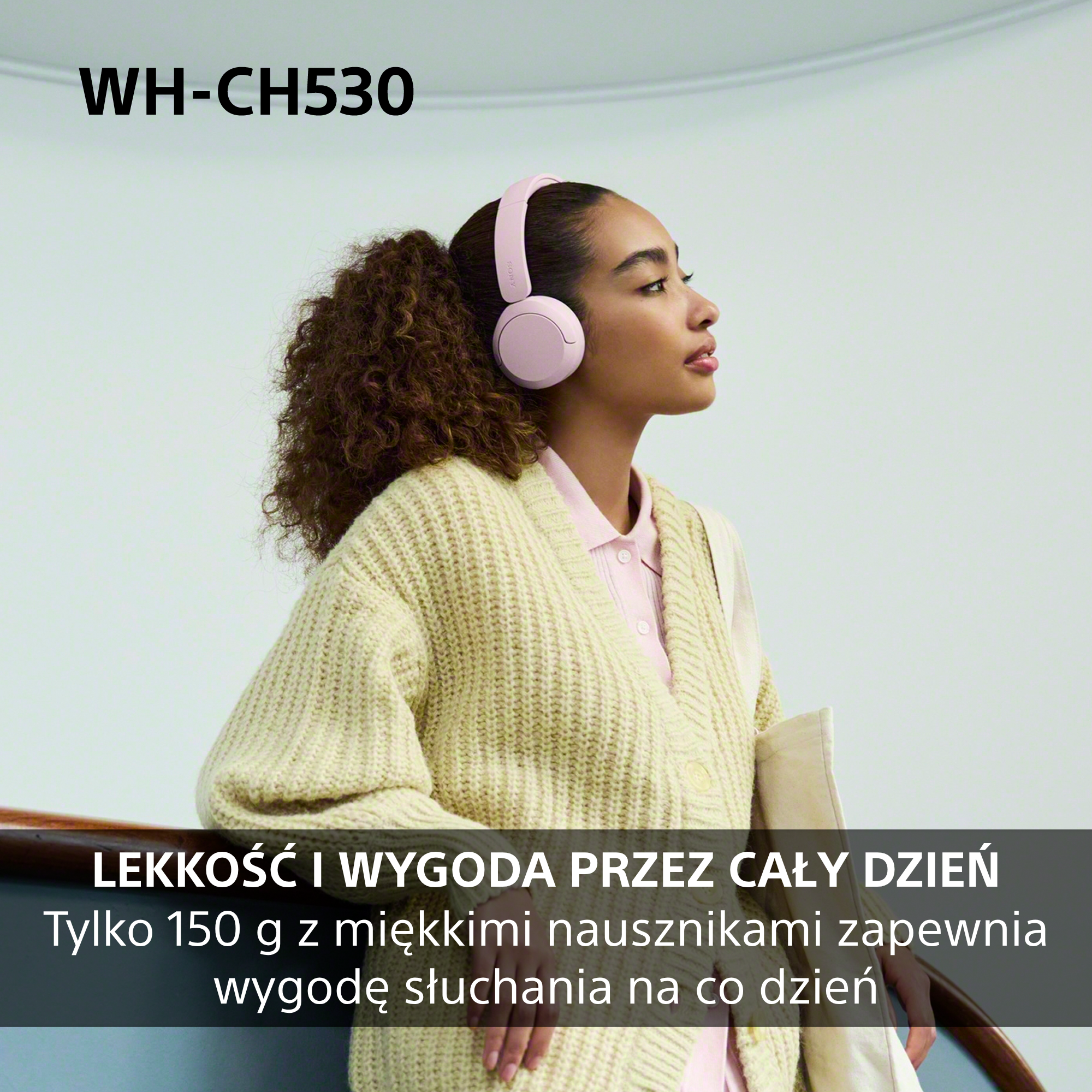 Kobieta w różowych słuchawkach, jasnym swetrze z dzianiny i kręconymi włosami na neutralnym tle.