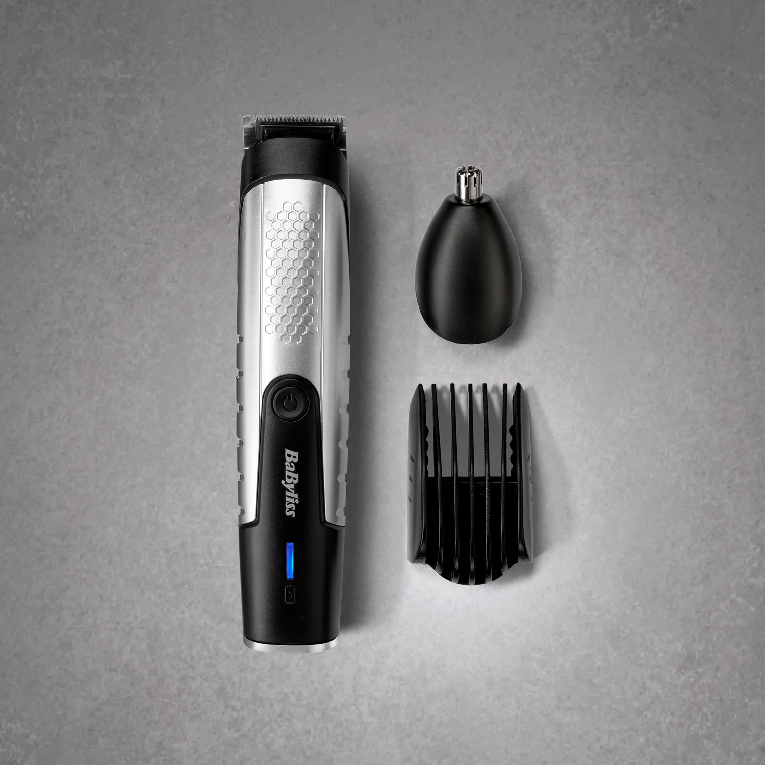 Regolabarba Babyliss con manico argento e nero, testina per naso e pettine guida su sfondo grigio.