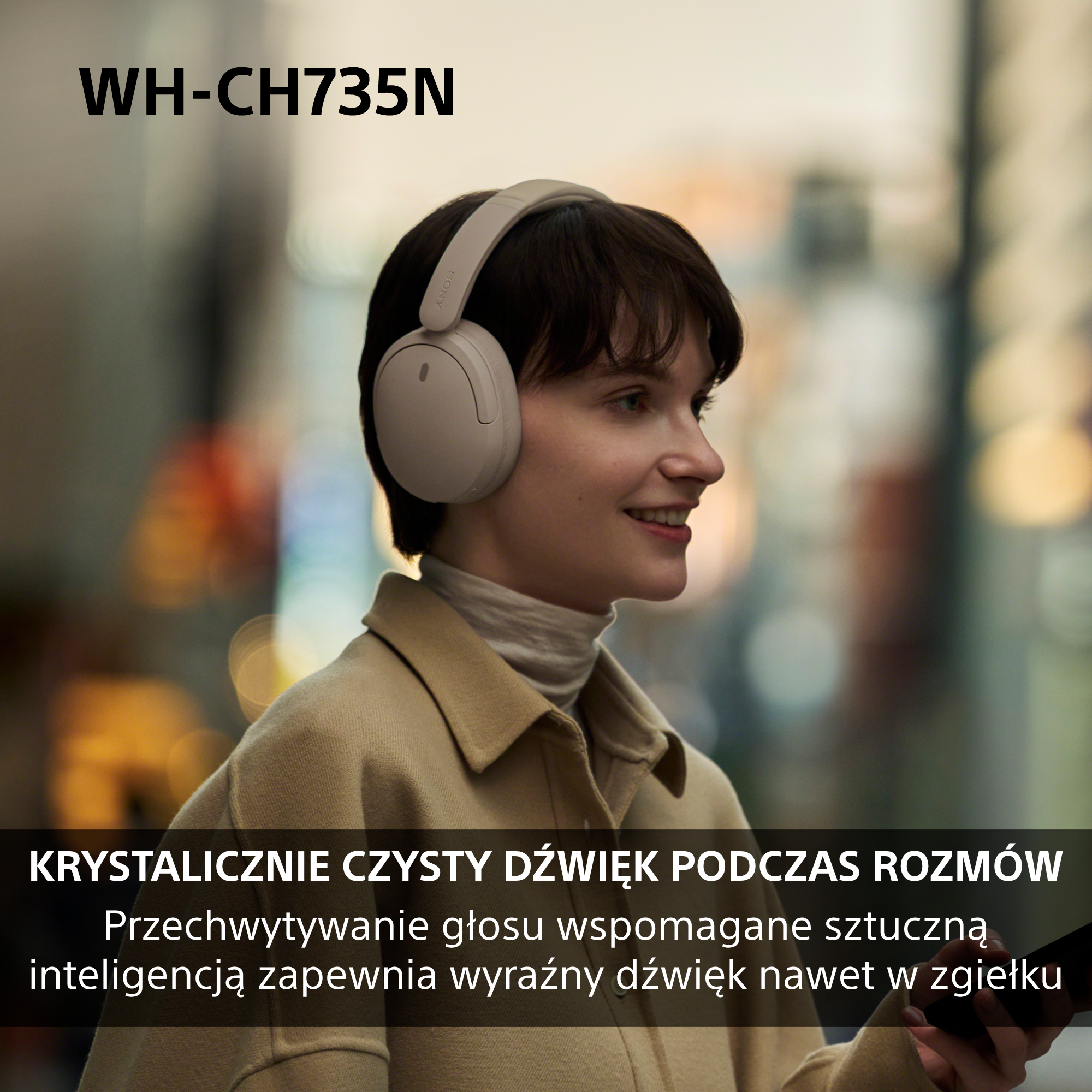 Młoda kobieta w beżowych słuchawkach uśmiecha się na ruchliwej ulicy.