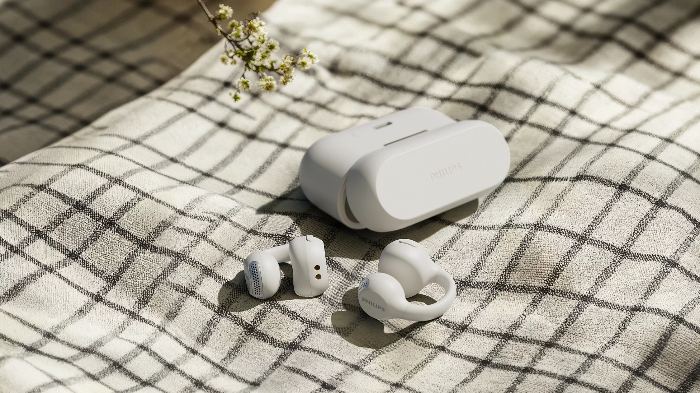 Écouteurs sans fil Philips blancs et étui de charge sur une couverture à carreaux avec de petites fleurs.