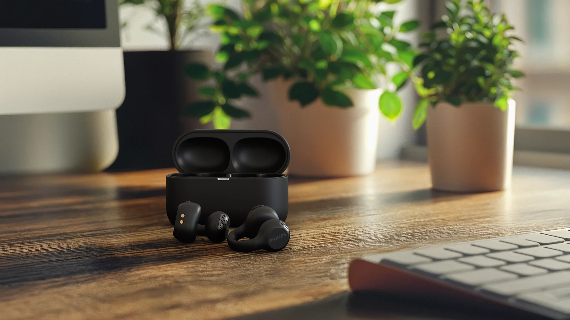 Écouteurs sans fil Philips noirs devant leur étui de chargement ouvert sur un bureau en bois avec des plantes en pot.