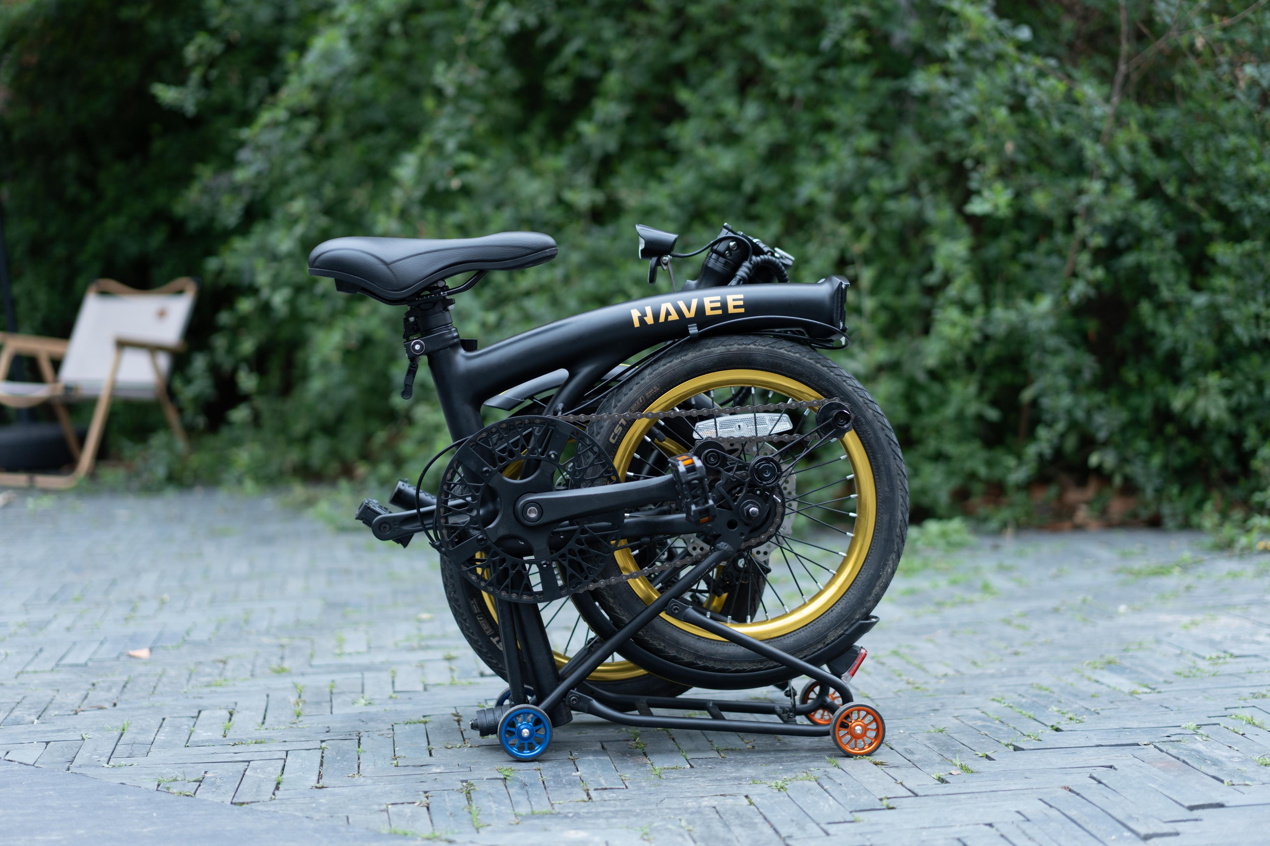 Ein zusammengeklapptes schwarzes Navee E-Bike mit goldenen Akzenten steht auf einem Ständer im Freien.