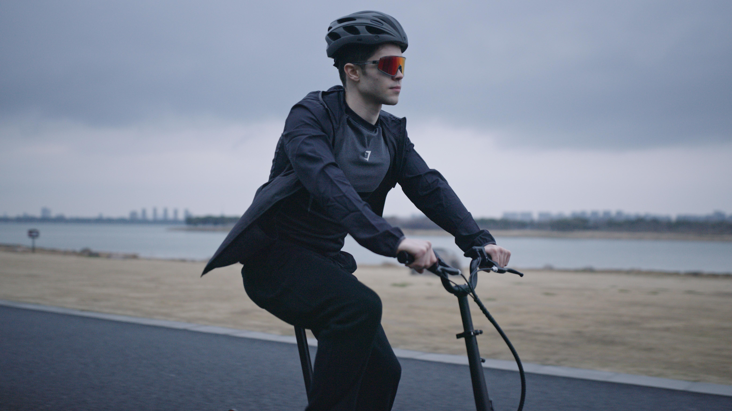 Ein Mann mit Helm und Brille fährt auf einer asphaltierten Straße nahe eines Flusses.