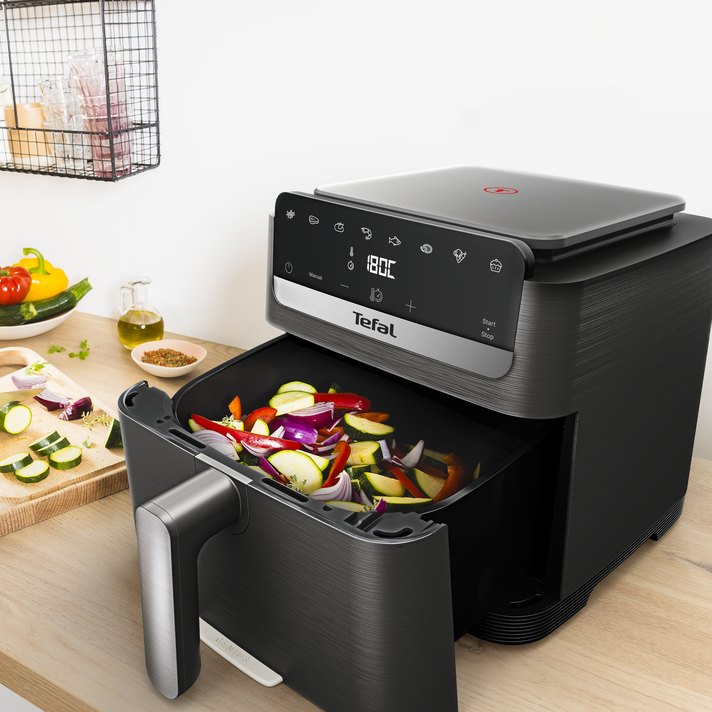 Egy fekete Tefal légsütő fa munkalapon, a nyitott fiókja tele van vágott zöldségekkel.