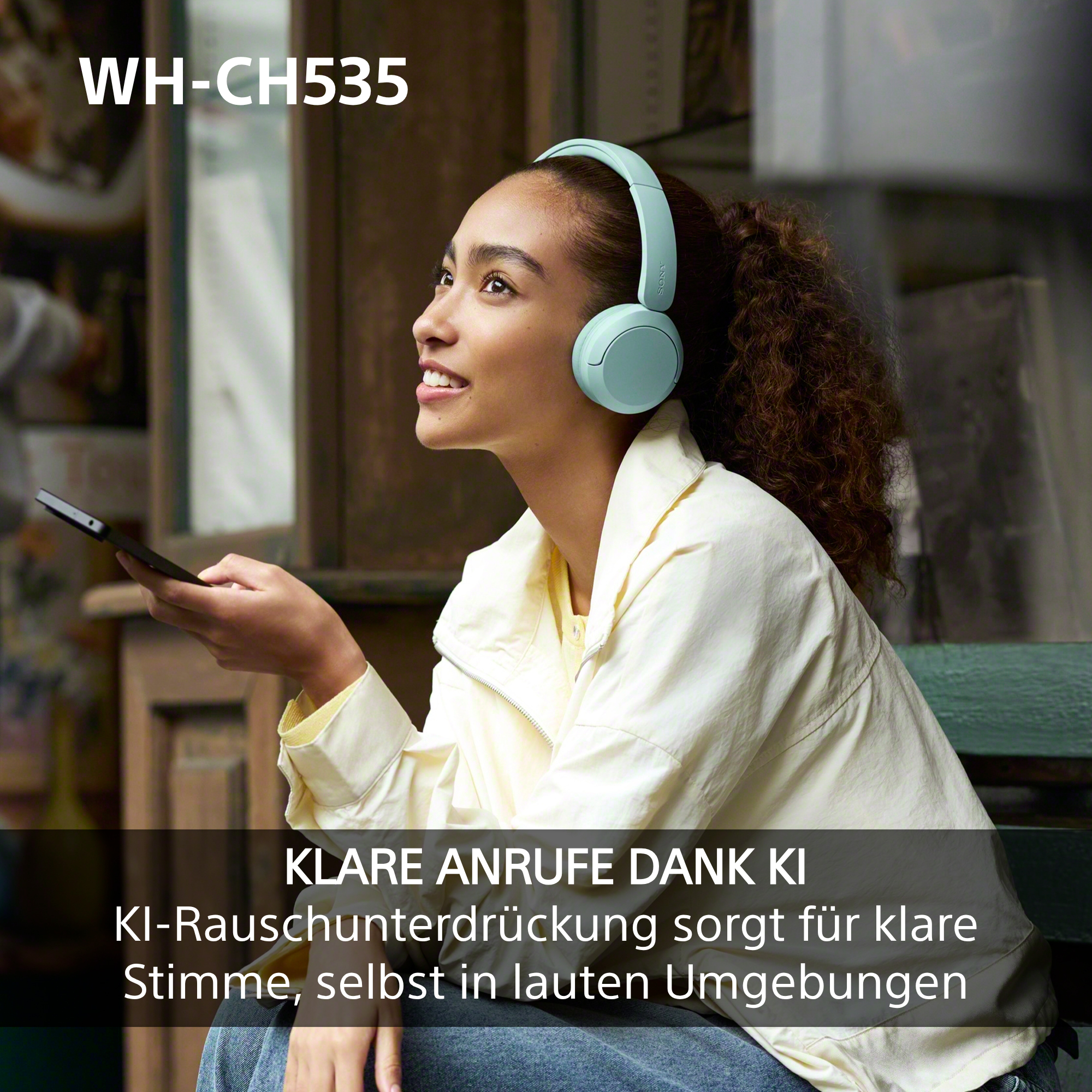 Frau mit hellblauen Kopfhörern und Smartphone lächelt und telefoniert in einem Café.