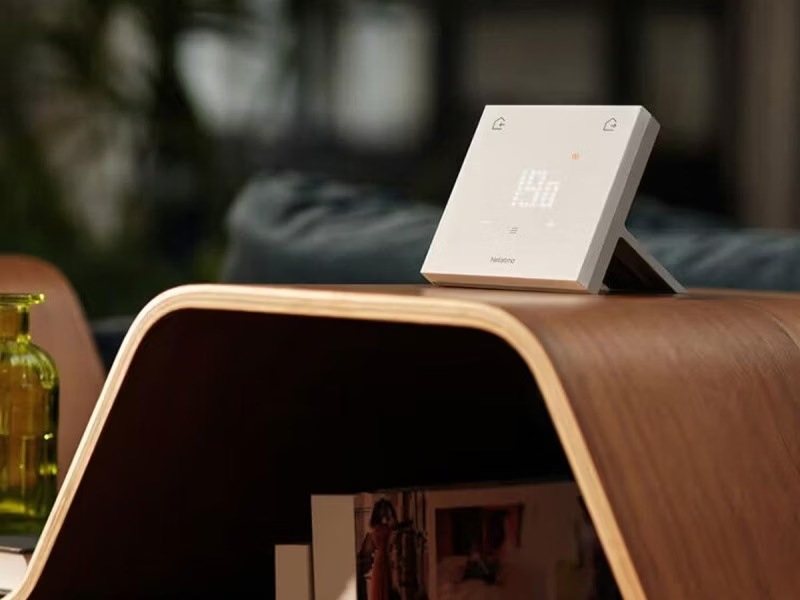 Un termostato inteligente blanco con pantalla digital se encuentra en una mesa de madera curva.