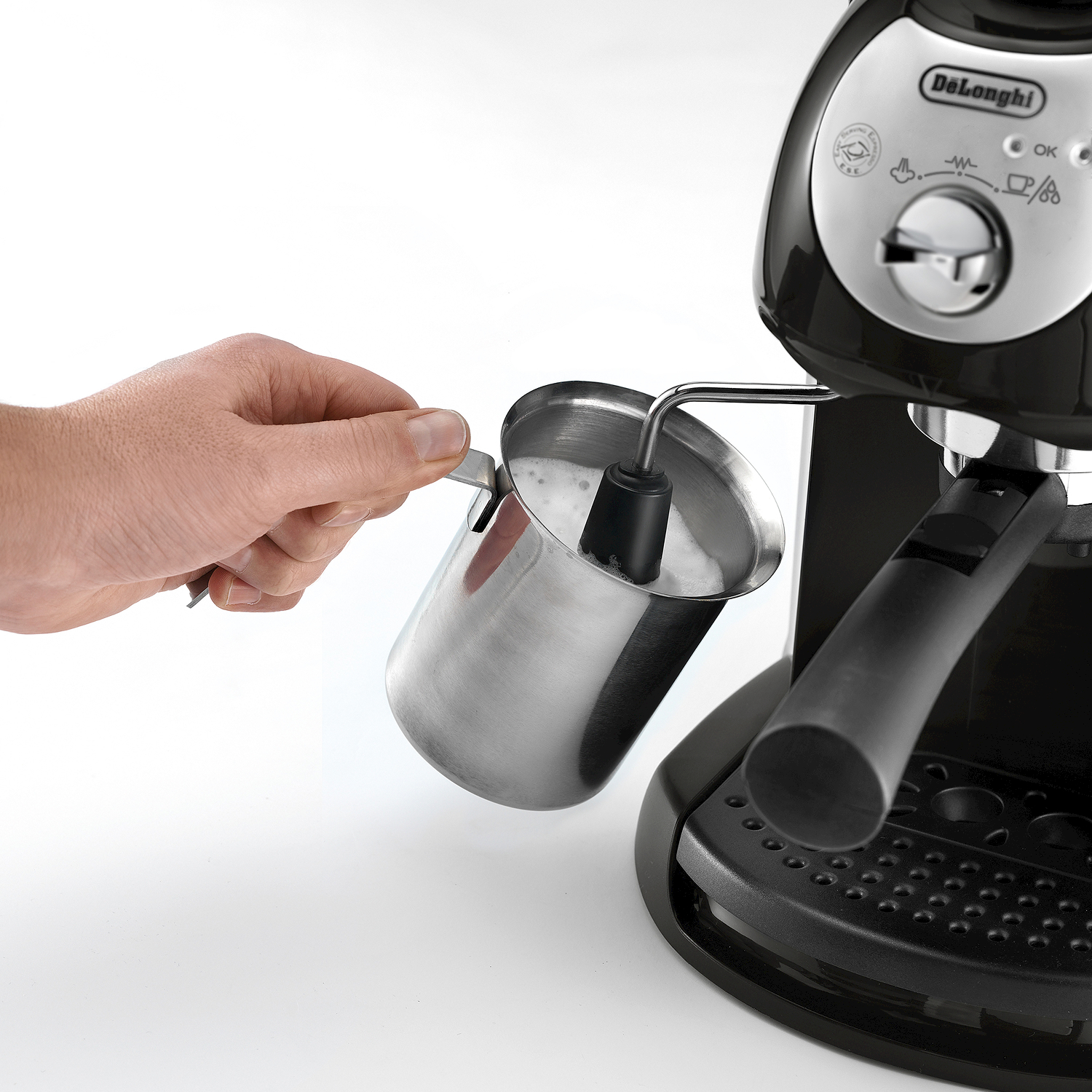 Una mano tiene una lattiera sotto il beccuccio del vapore di una macchina da caffè.