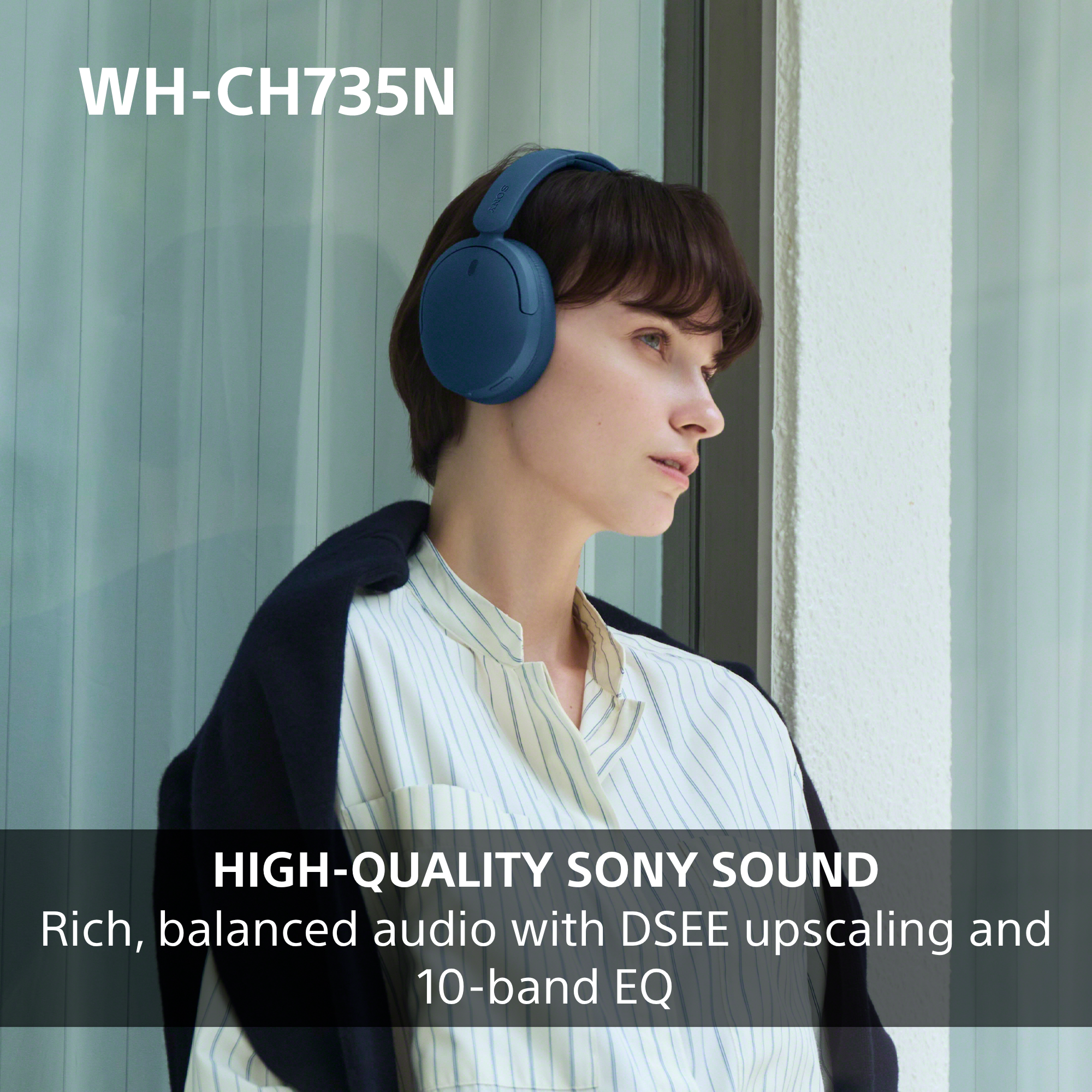 Eine Frau mit kurzen dunklen Haaren trägt blaue Sony-Kopfhörer und ein gestreiftes Hemd vor einem hellen Hintergrund.