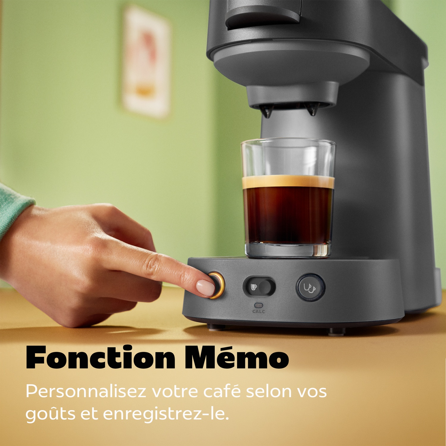 Une main appuie sur le bouton d'une machine à café grise avec une tasse de café.