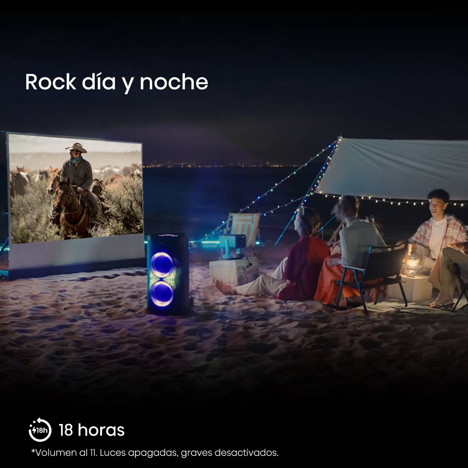 Amigos ven una película en una pantalla en la playa de noche, junto a un altavoz.