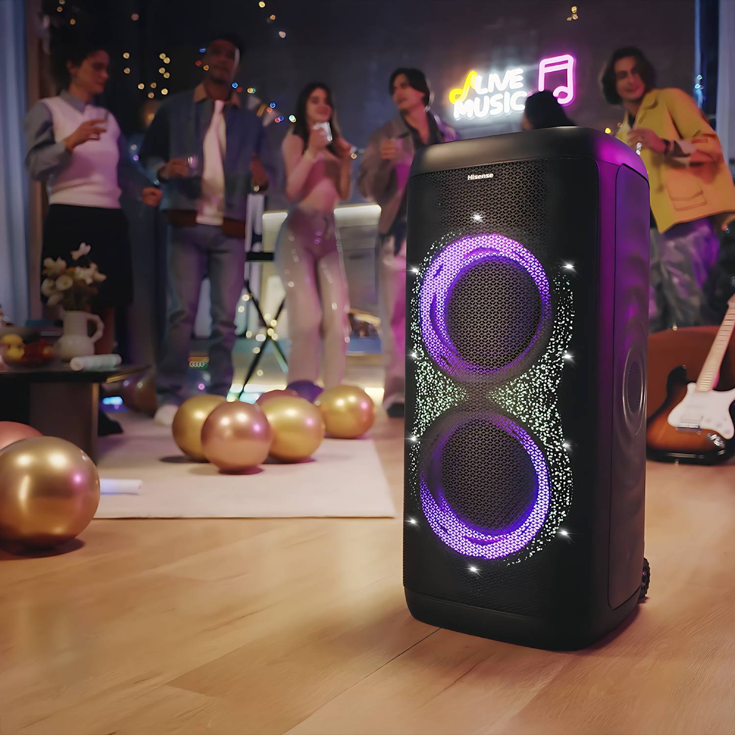 Un gran altavoz negro de fiesta con luces LED coloridas en primer plano, con personas celebrando al fondo.