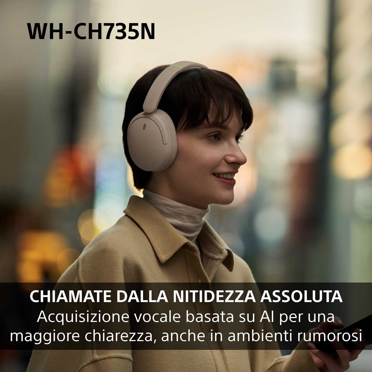Donna sorridente con cuffie e giacca beige su sfondo sfocato, tiene in mano lo smartphone.