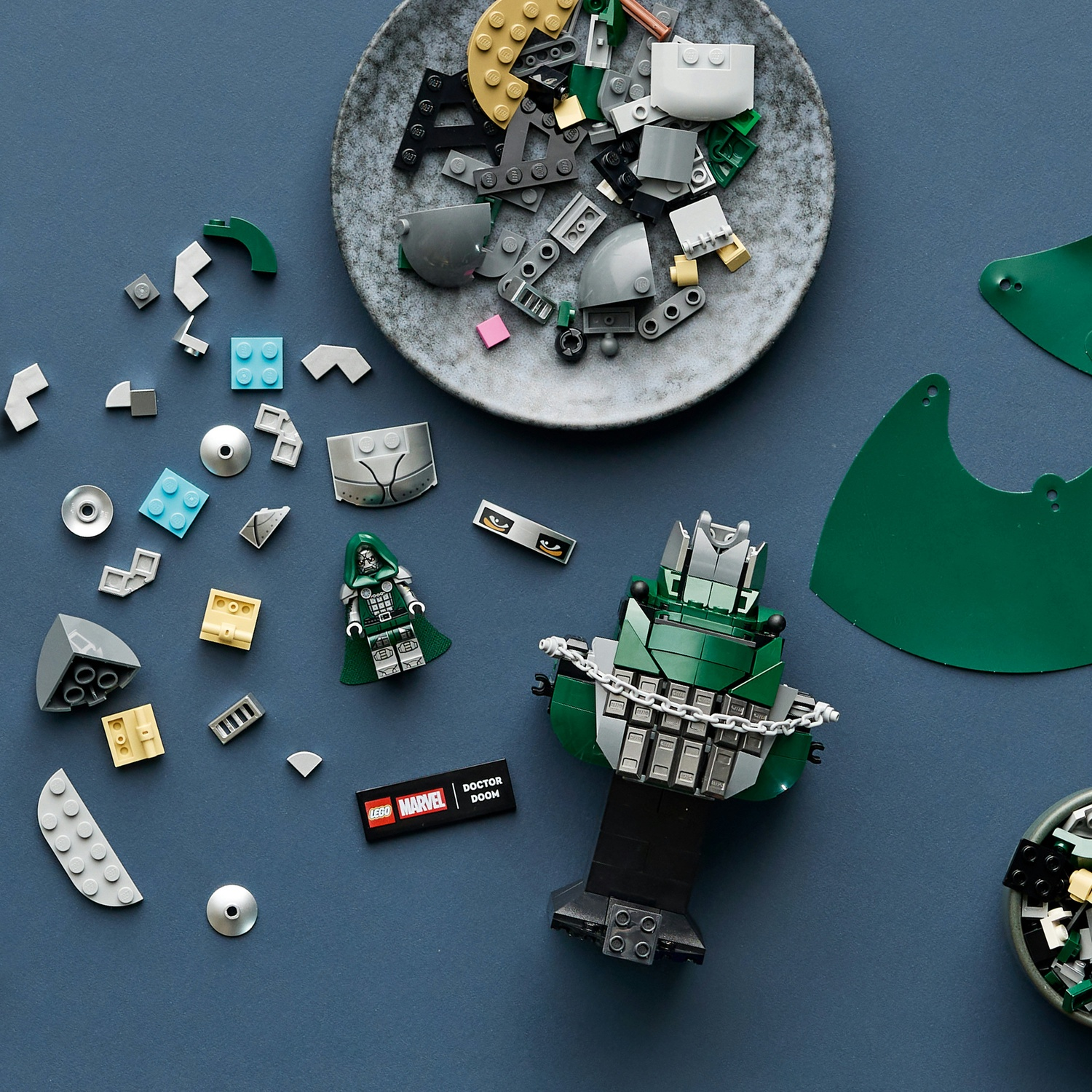 Kit di costruzione Lego Marvel Doctor Doom con pezzi sfusi, piastre e una minifigure su sfondo blu.