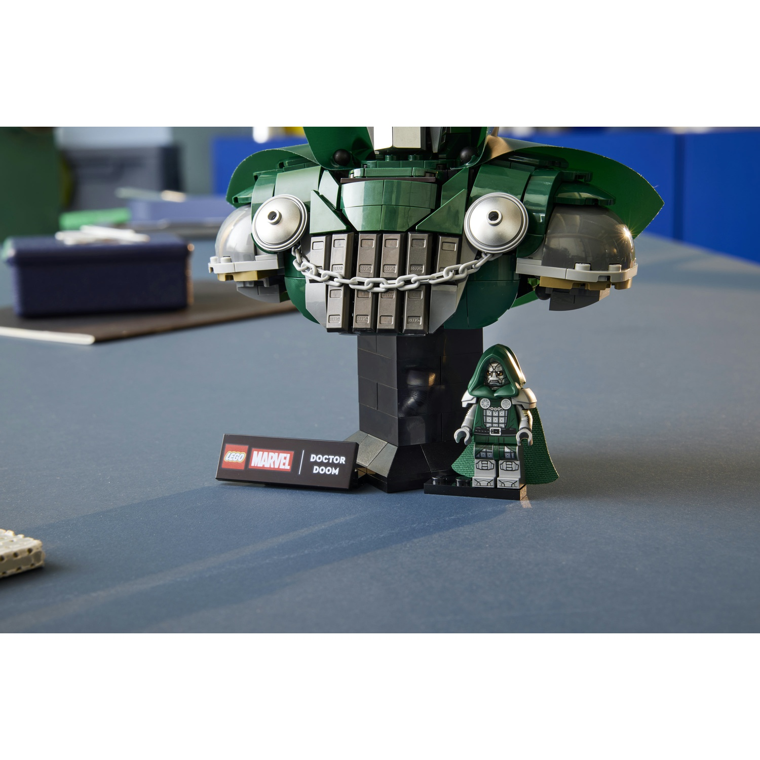 Busto Lego Doctor Doom con minifigura e targhetta su tavolo blu.