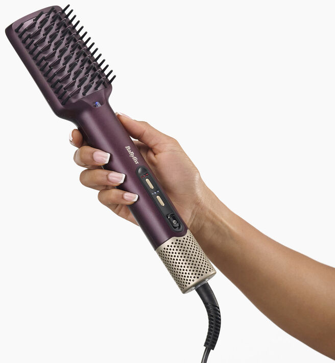 Une main tient une brosse soufflante BaByliss sombre avec un détail doré sur un fond blanc.