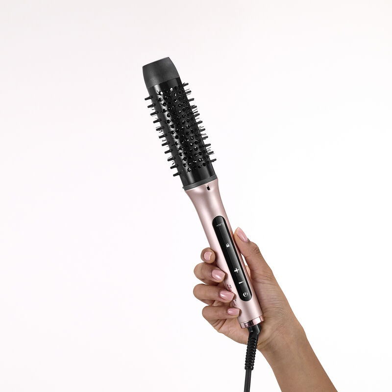 Une main tient une brosse soufflante or rose avec une tête noire et un affichage numérique sur fond blanc.