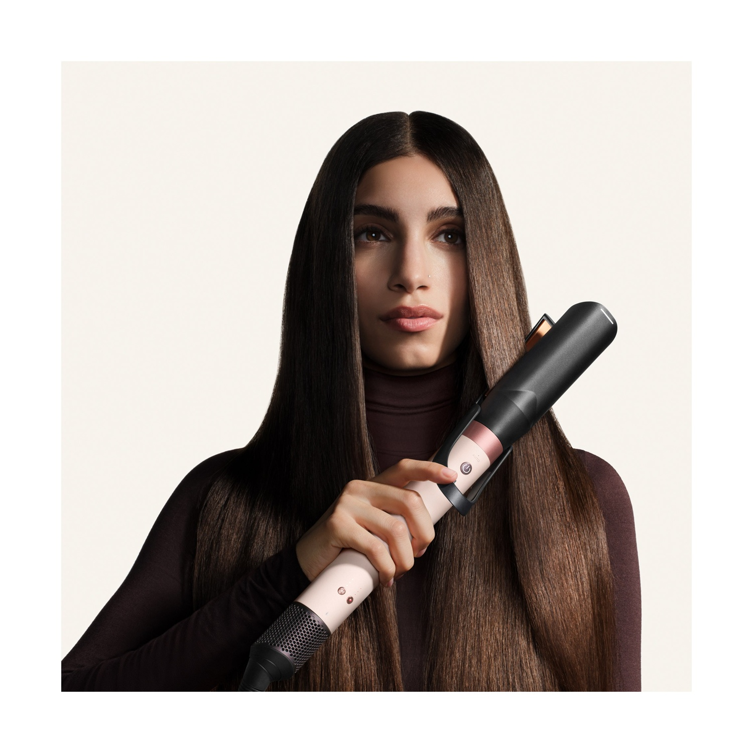 Una donna con lunghi capelli castani tiene in mano uno styler nero e rosa su sfondo chiaro.
