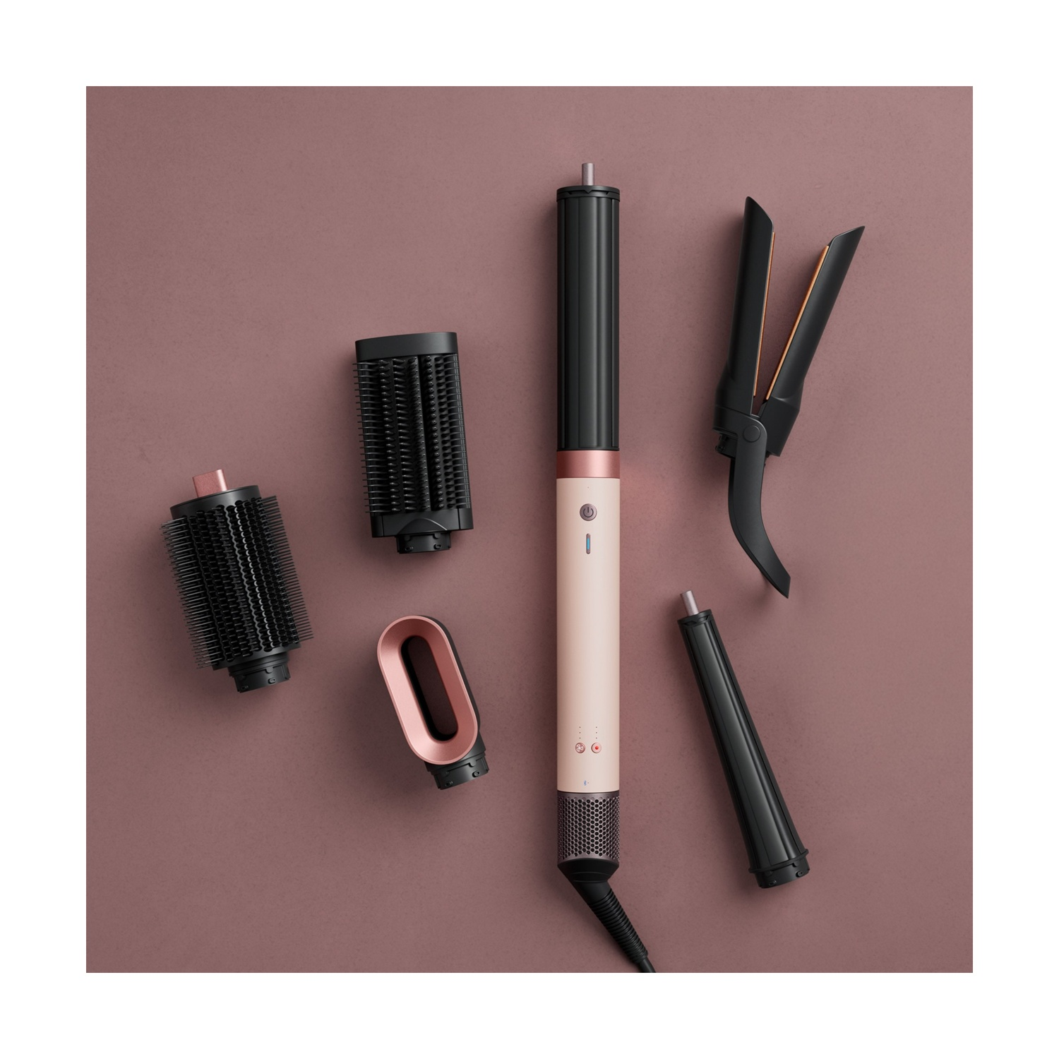 Uno styler per capelli rosa e nero con vari accessori disposti su una superficie rosa.