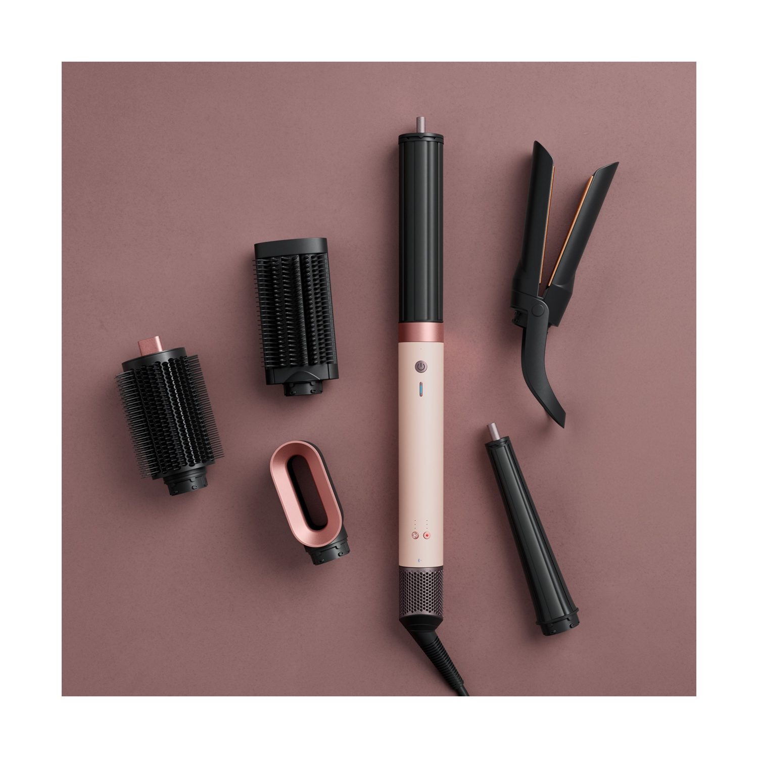 Uno styler per capelli rosa con vari accessori su sfondo rosa.
