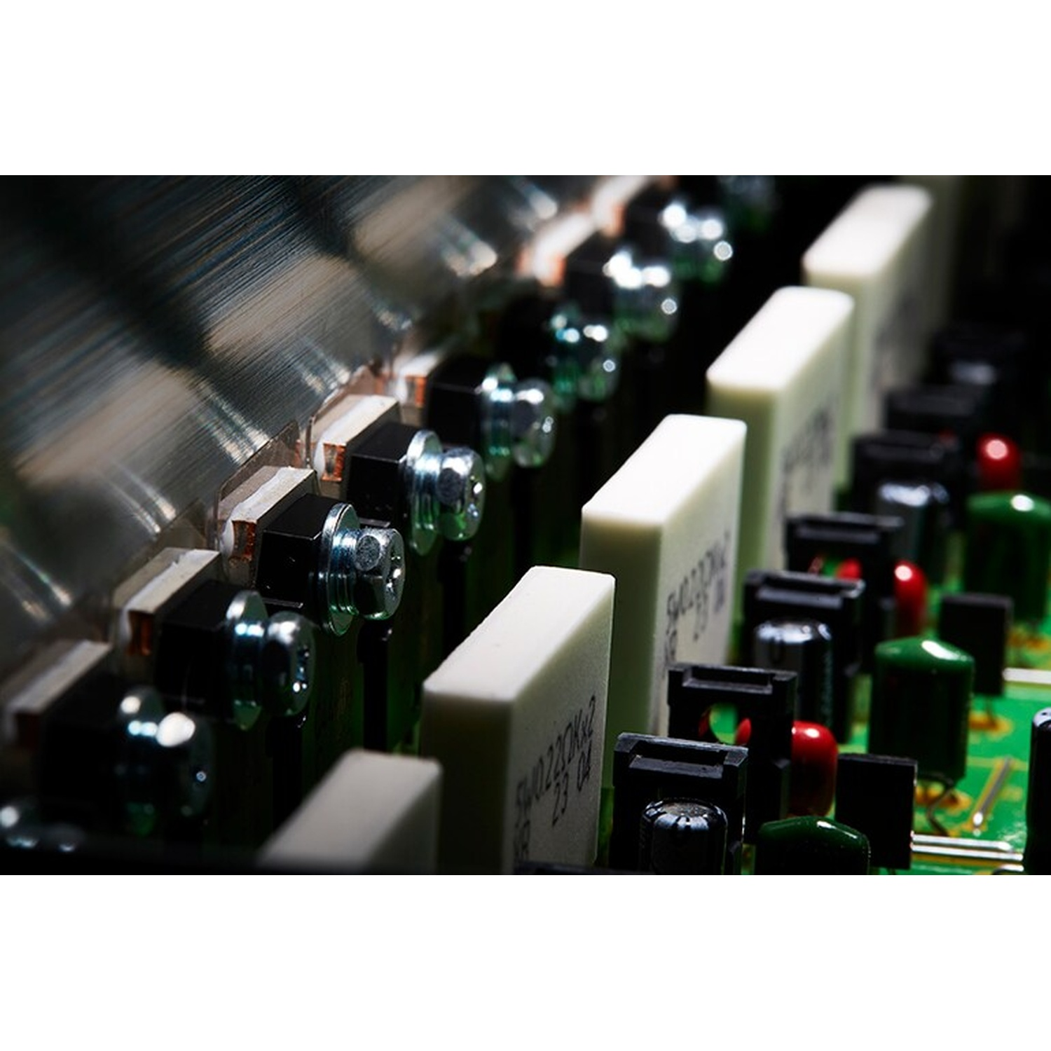 Primo piano di un circuito stampato verde con componenti elettronici, viti e dissipatori.