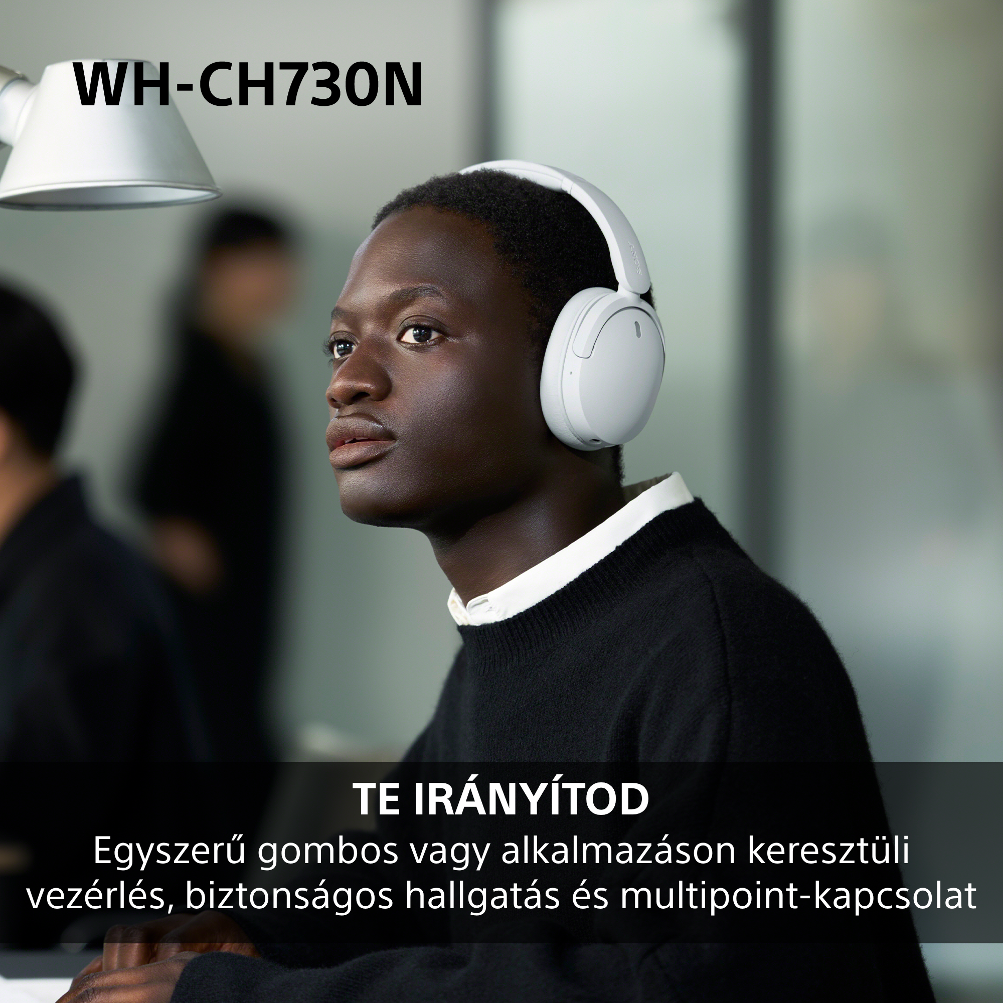 Fiatal férfi fehér fejhallgatóban egy modern irodában.