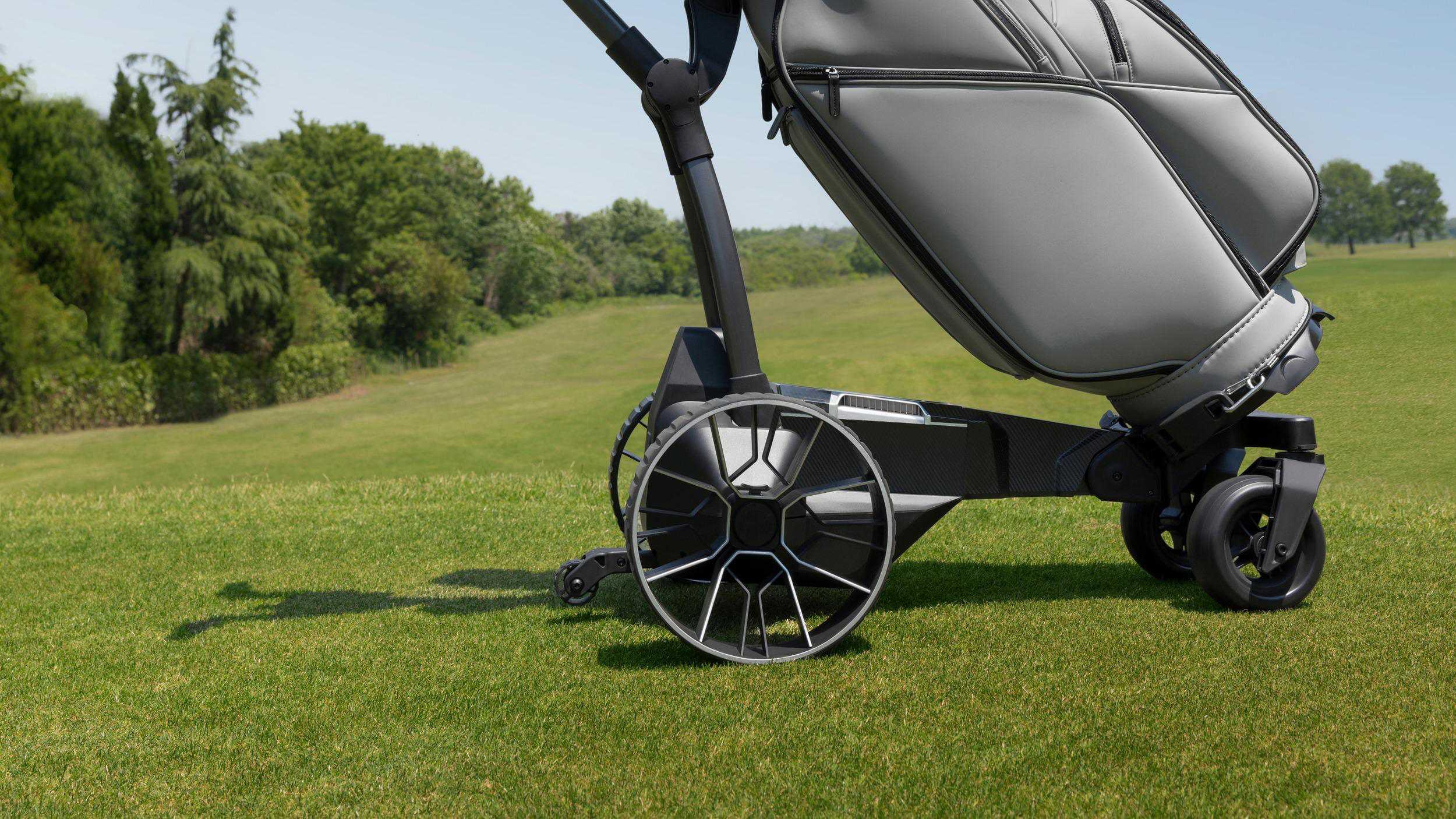 Ein moderner grauer Golfcaddy mit passender Tasche steht auf einem sonnigen grünen Golfplatz.