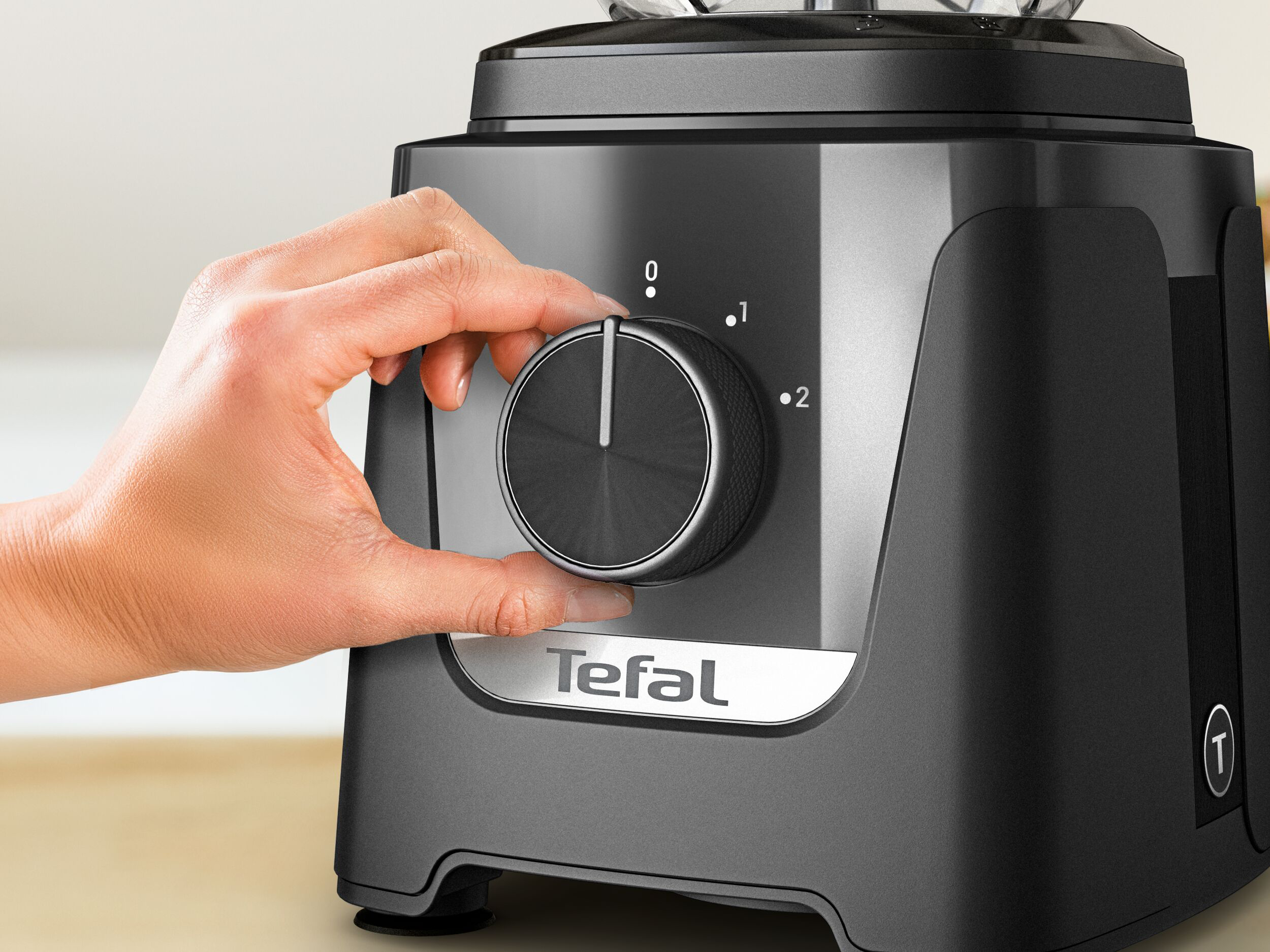 Egy kéz elforgatja a sebességszabályozó gombot egy fekete Tefal turmixgépen.