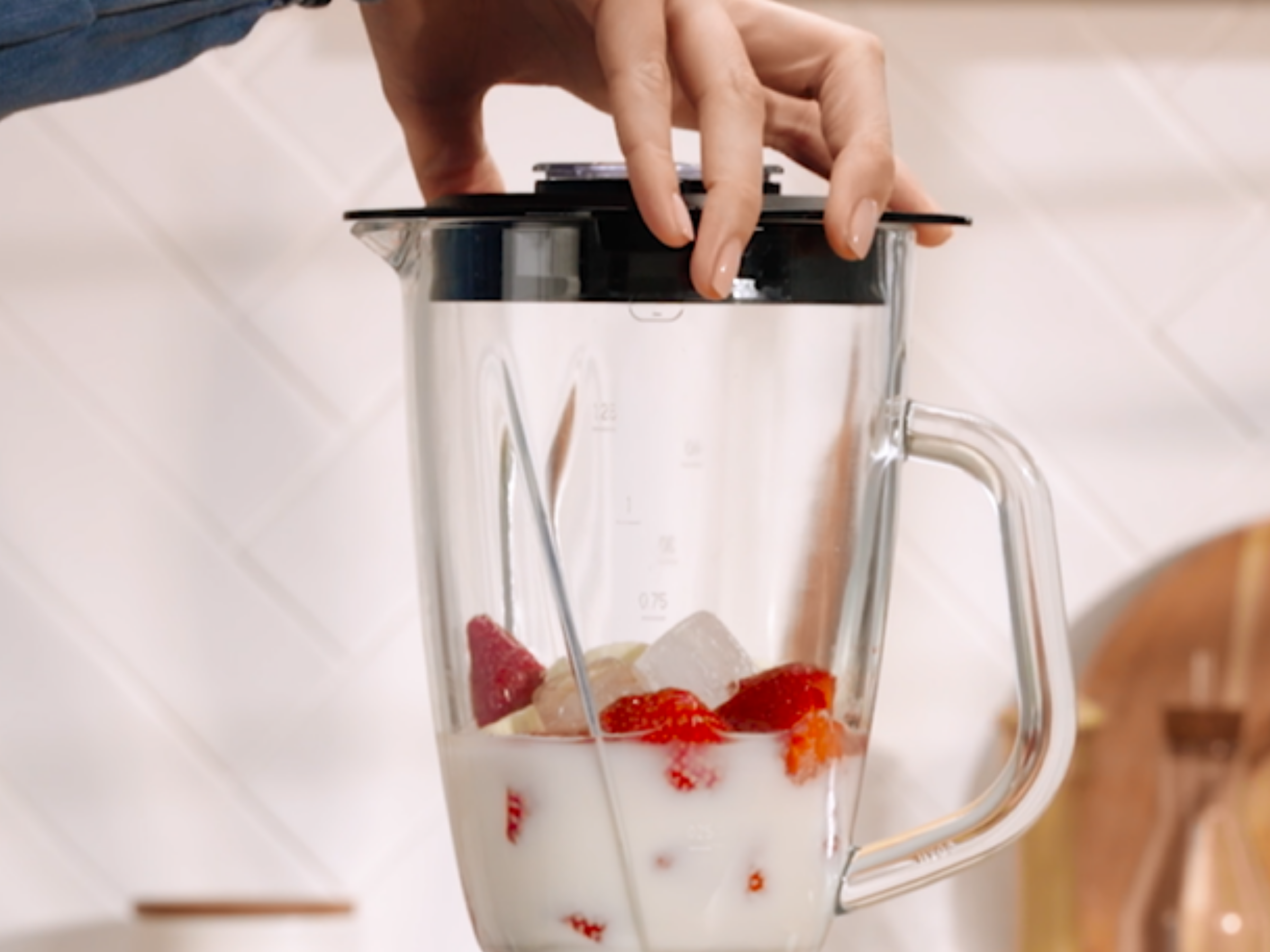 Egy személy ráteszi a fedőt a tejet, epret és jégkockát tartalmazó üveg turmixgépre.