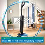 Ein schwarzer Staubsauger steht in einem hellen Wohnzimmer mit Texten und Grafiken.