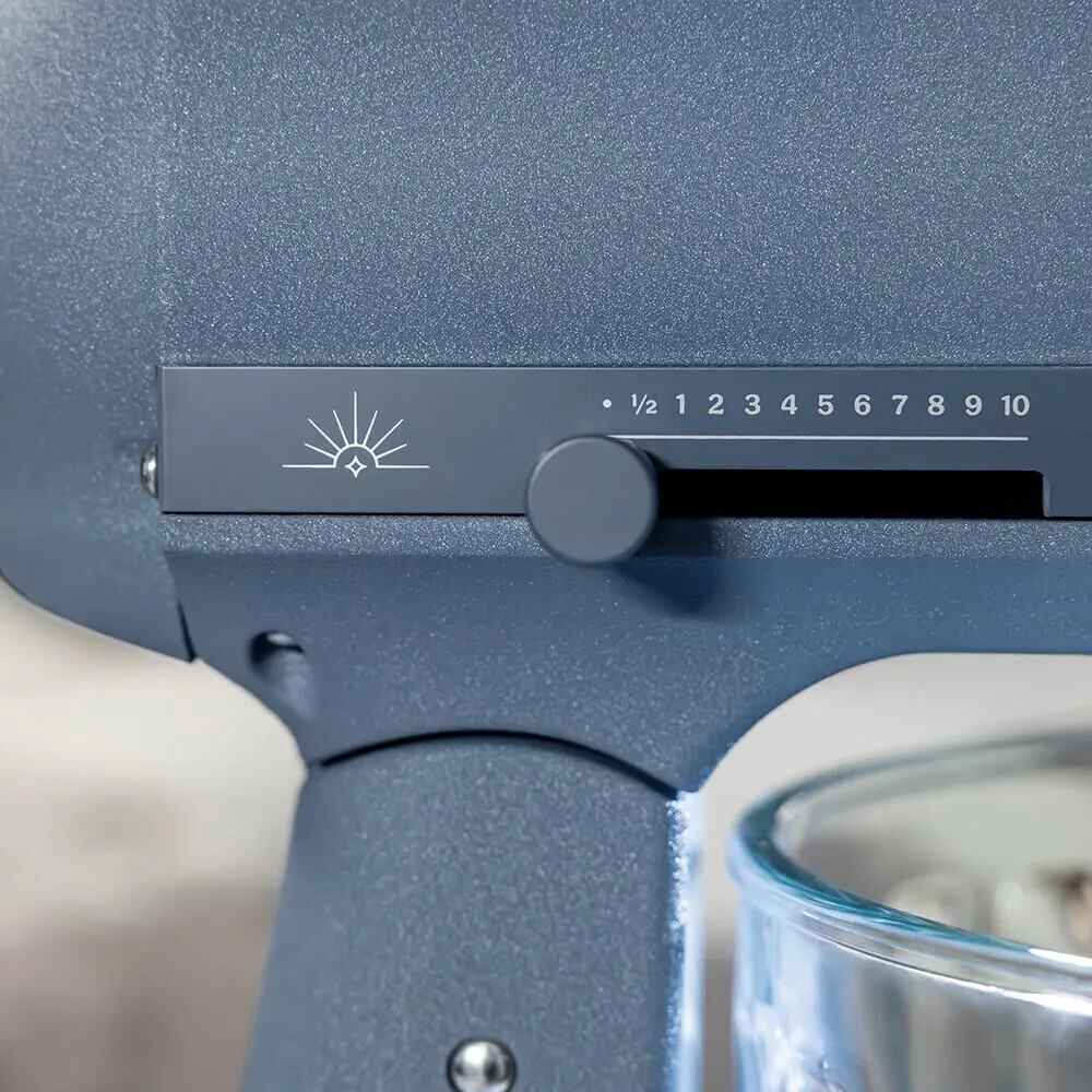 Nahaufnahme des blauen Bedienfelds einer Küchenmaschine mit Geschwindigkeitsregler und Sonnensymbol.